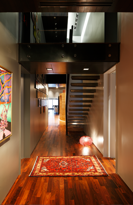 Modern penthouse hallway with steel stair, wooden floors, a colorful rug, staircase, artwork on the walls, and a glowing decorative light on the floor.