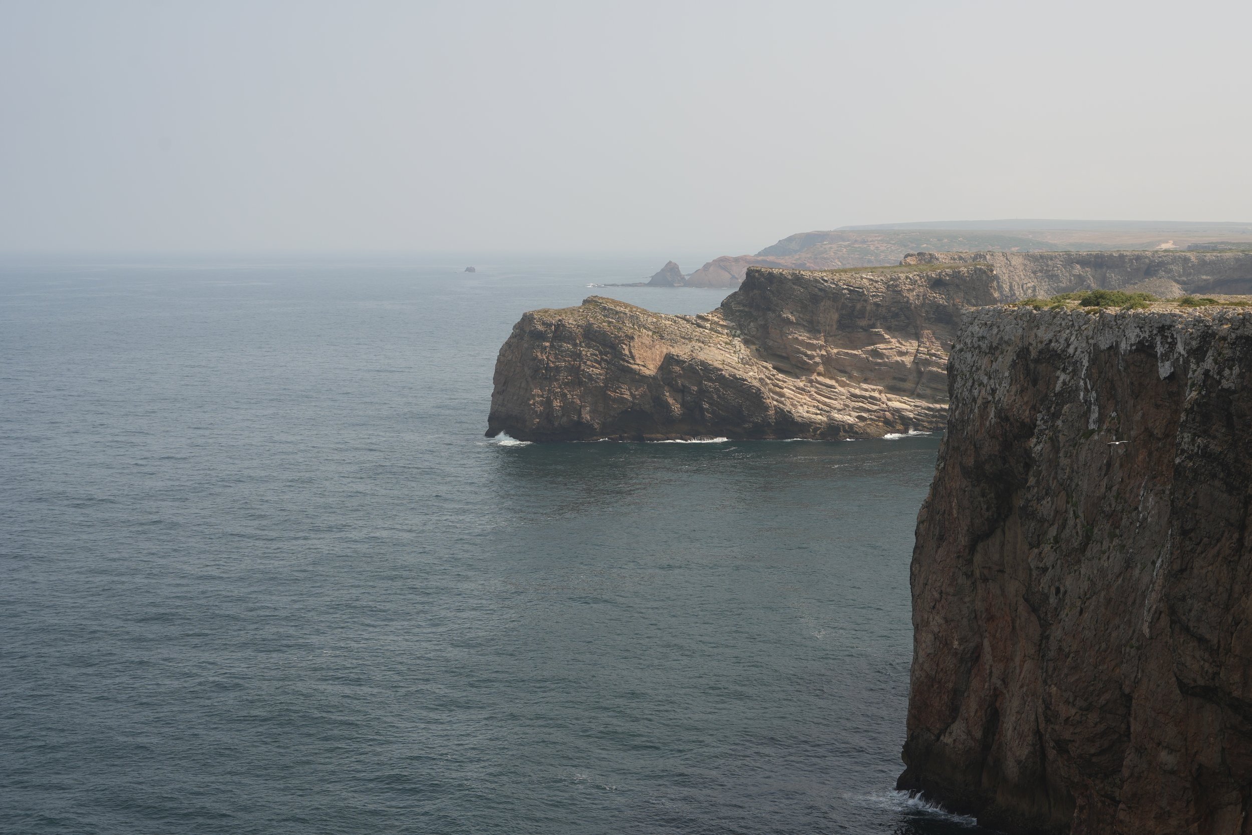 Klippen und Felsen an einer Küste mit dem Meer im Vordergrund und einer bewölkten Himmel.
