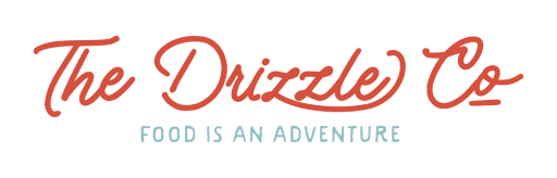 Text image with the words "The Drizzle Co" in red cursive font and "Food is an Adventure" in smaller blue font underneath.