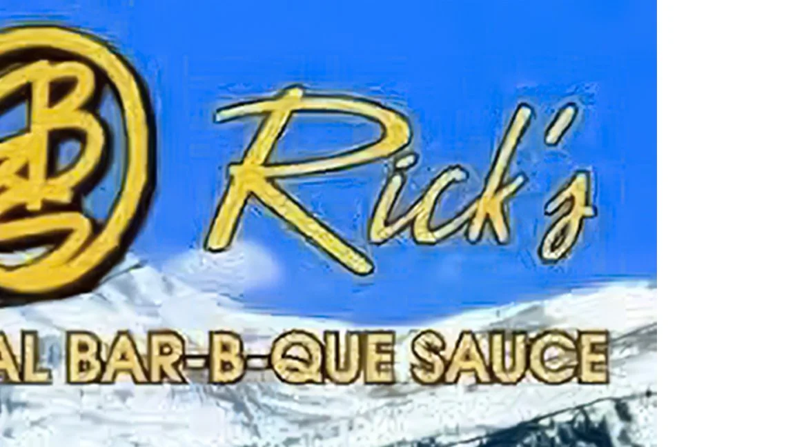 Sign for Rick's All Bar-B-Que Sauce against a mountain and sky background.