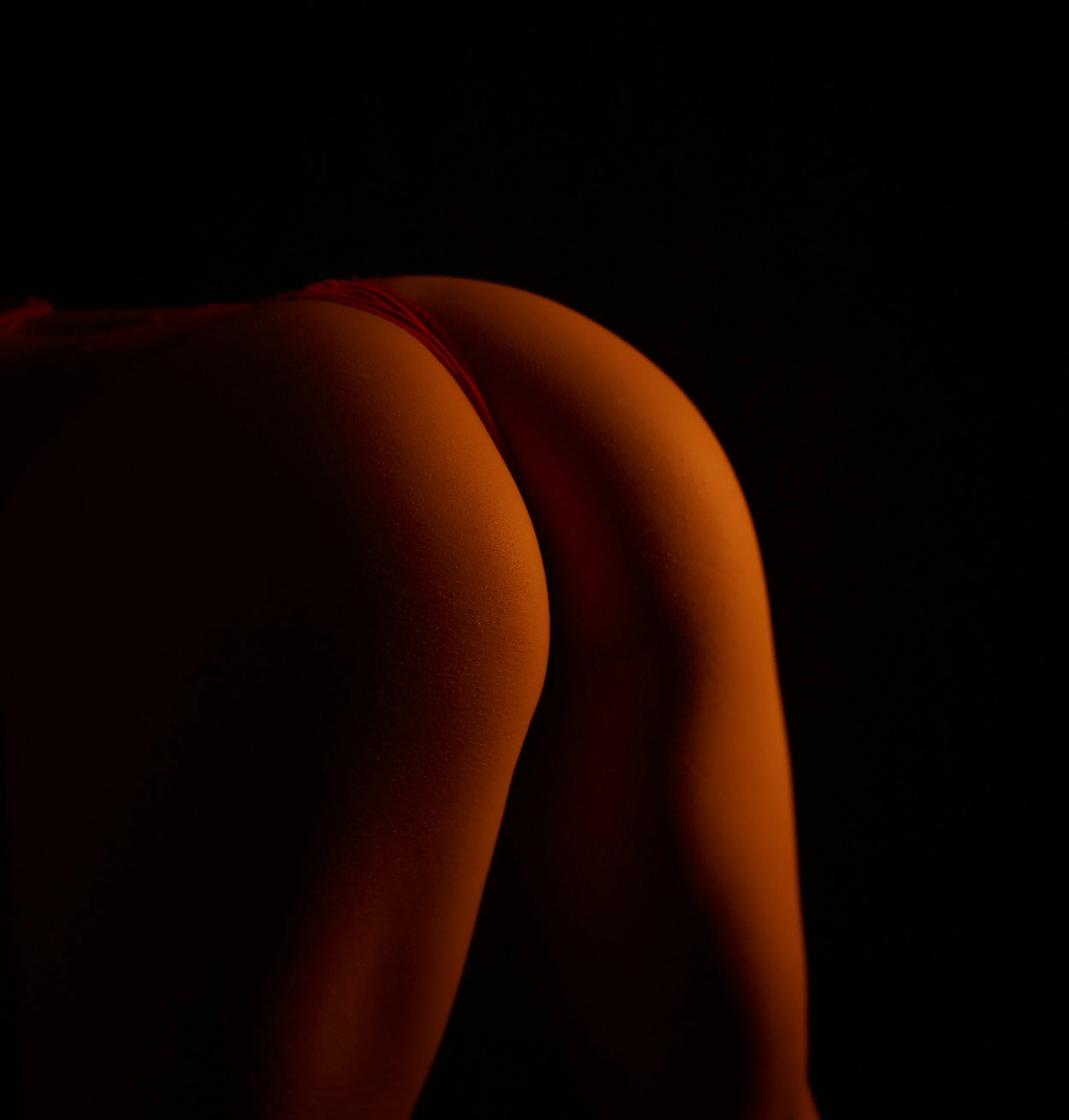 Close-up of person's backside, illuminated with warm lighting, against a dark background.