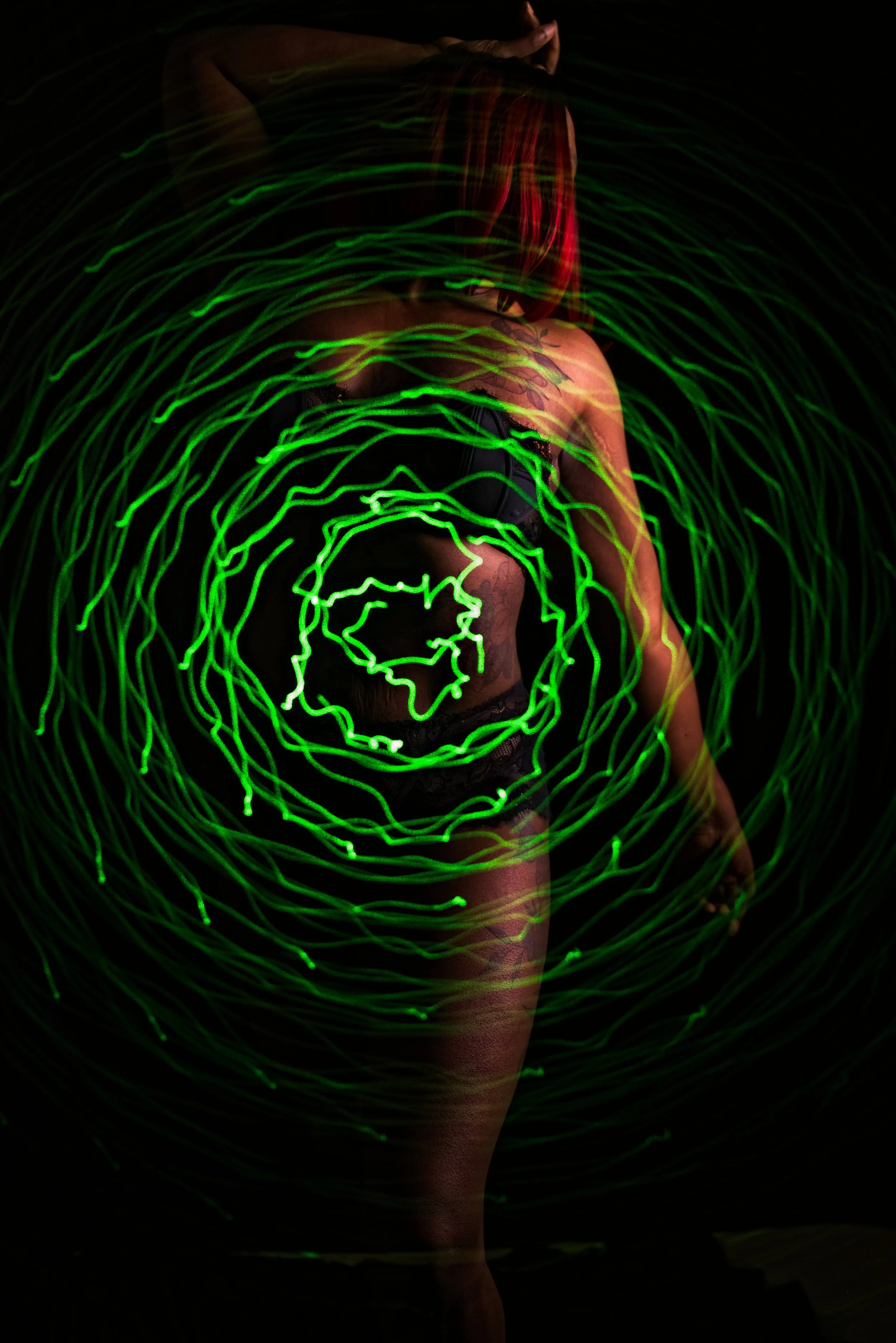 Person with red hair standing in front of a dark background, illuminated by swirling green light patterns.