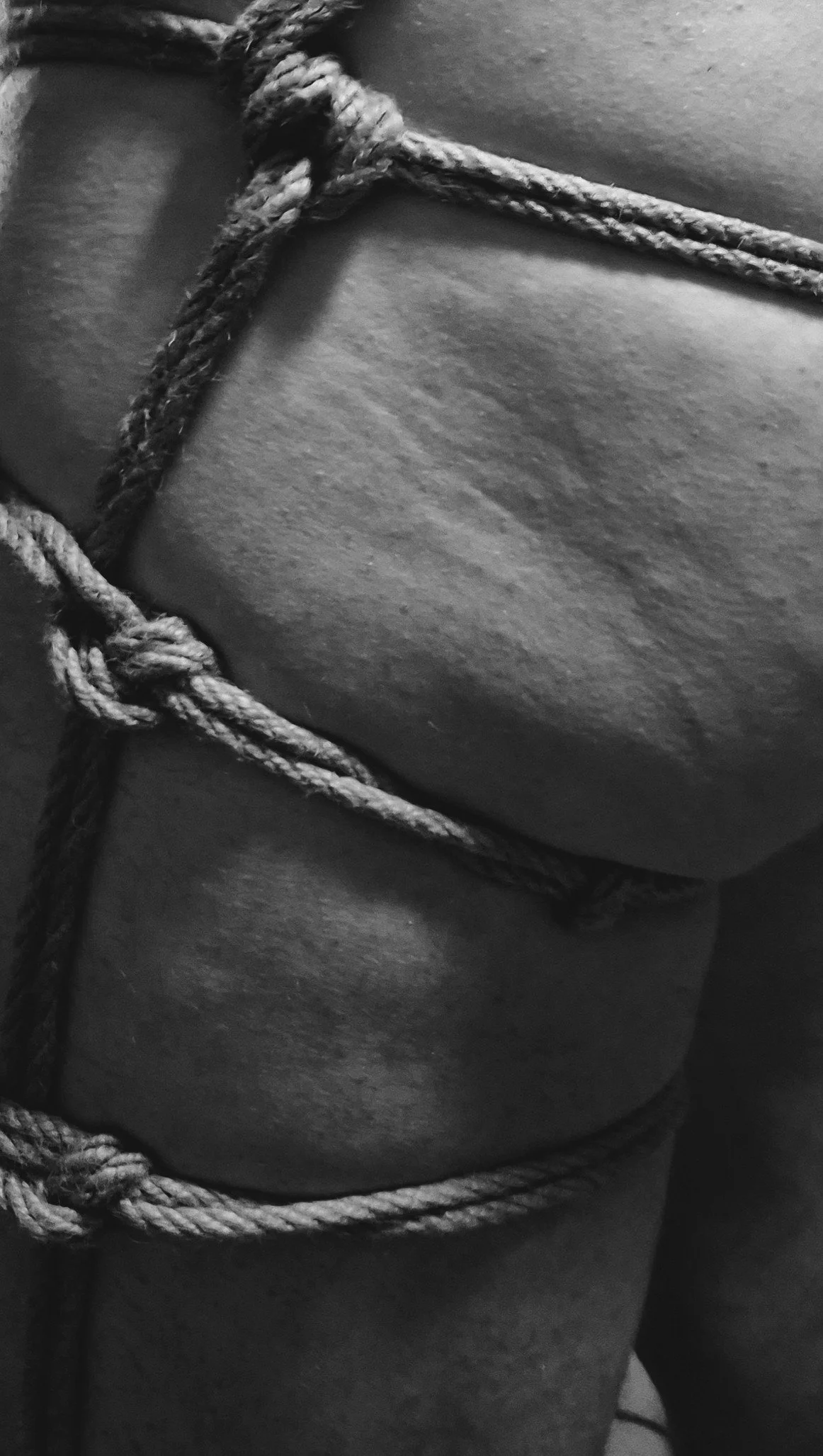 Close-up of a person's shoulder and upper arm, wrapped in a thick, textured rope. Black and white photograph emphasizing texture and contrast.