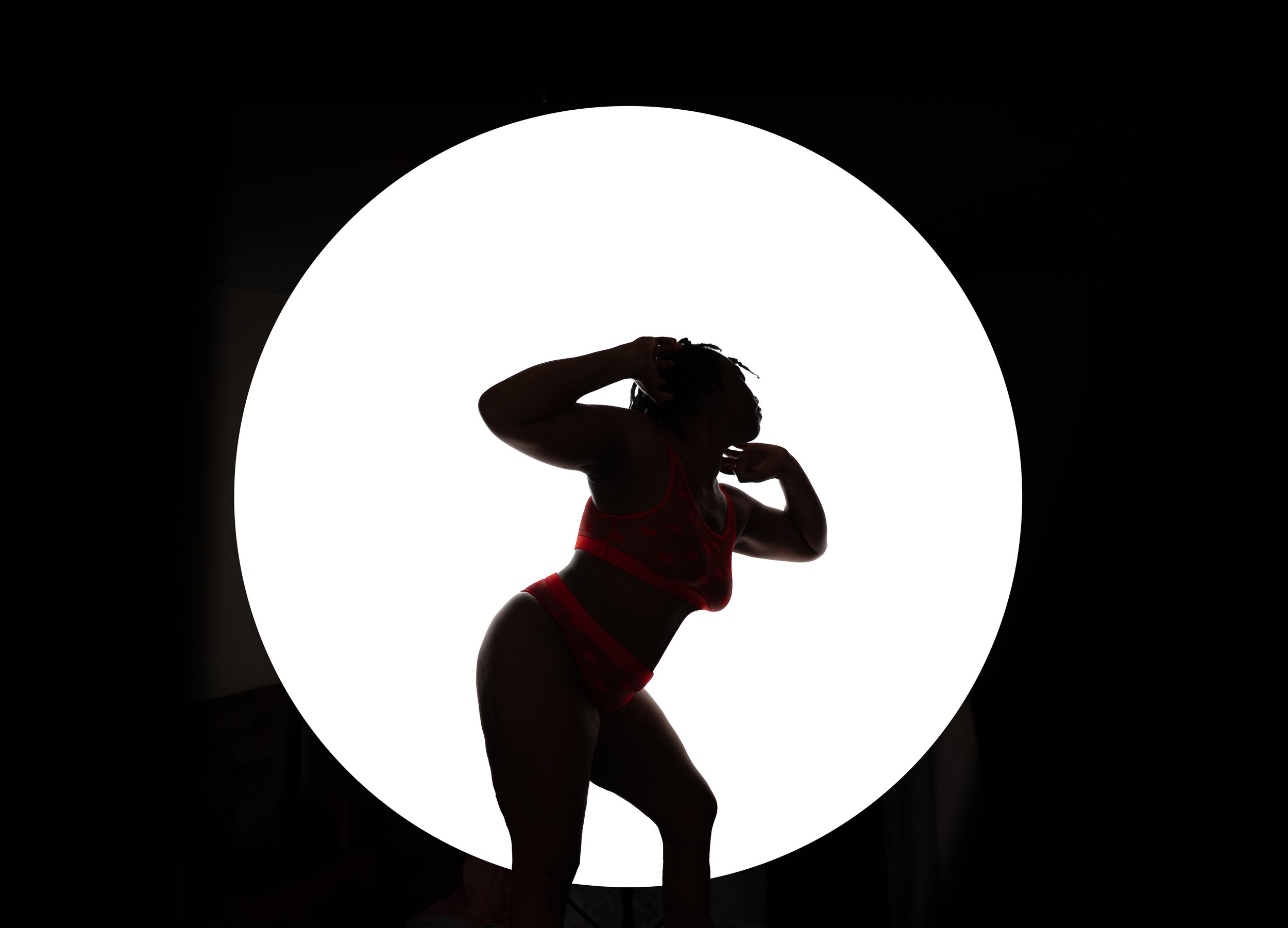 Silhouette of a woman in red lingerie striking a pose against a large circular bright white background.