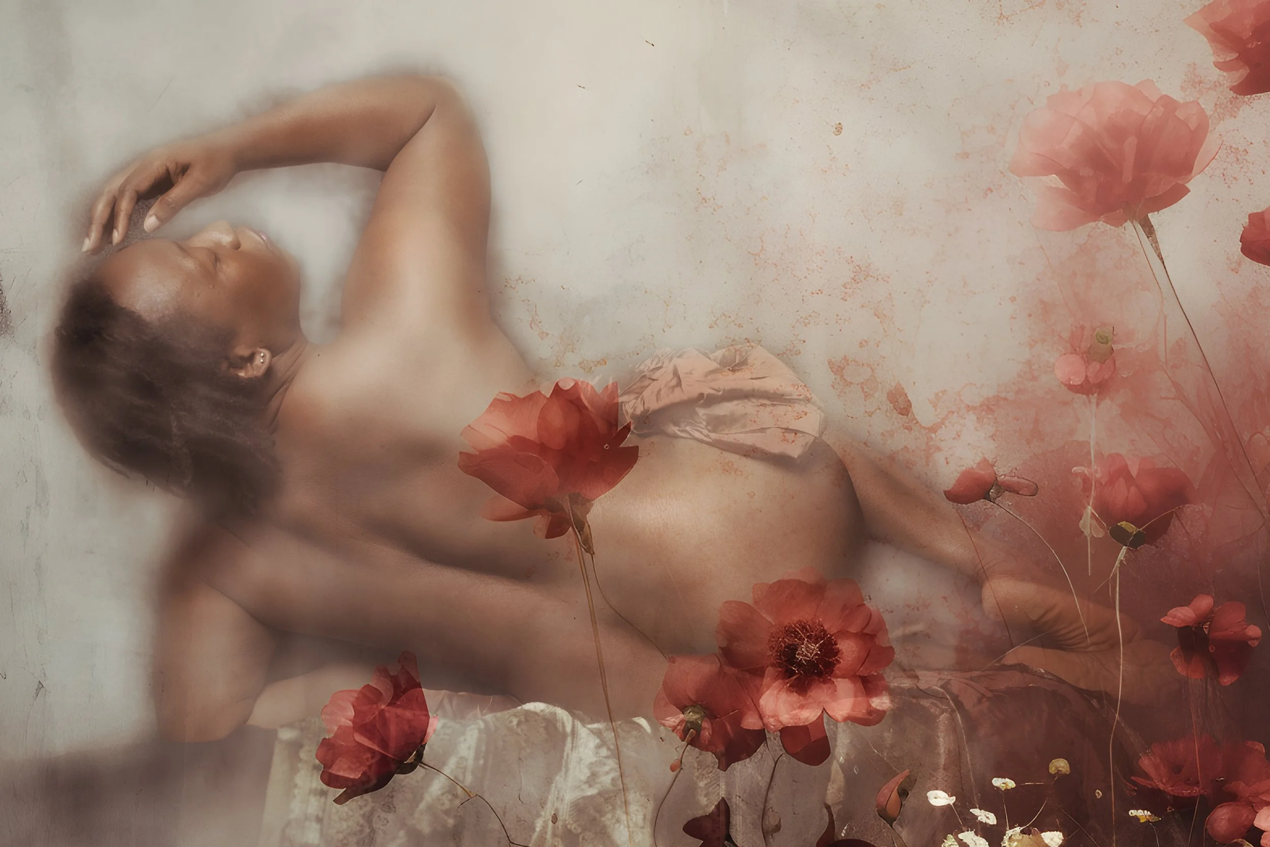 A person lying down with their eyes closed, surrounded by blooming red flowers with dark centers and floating petals, creating a dreamy, artistic scene.