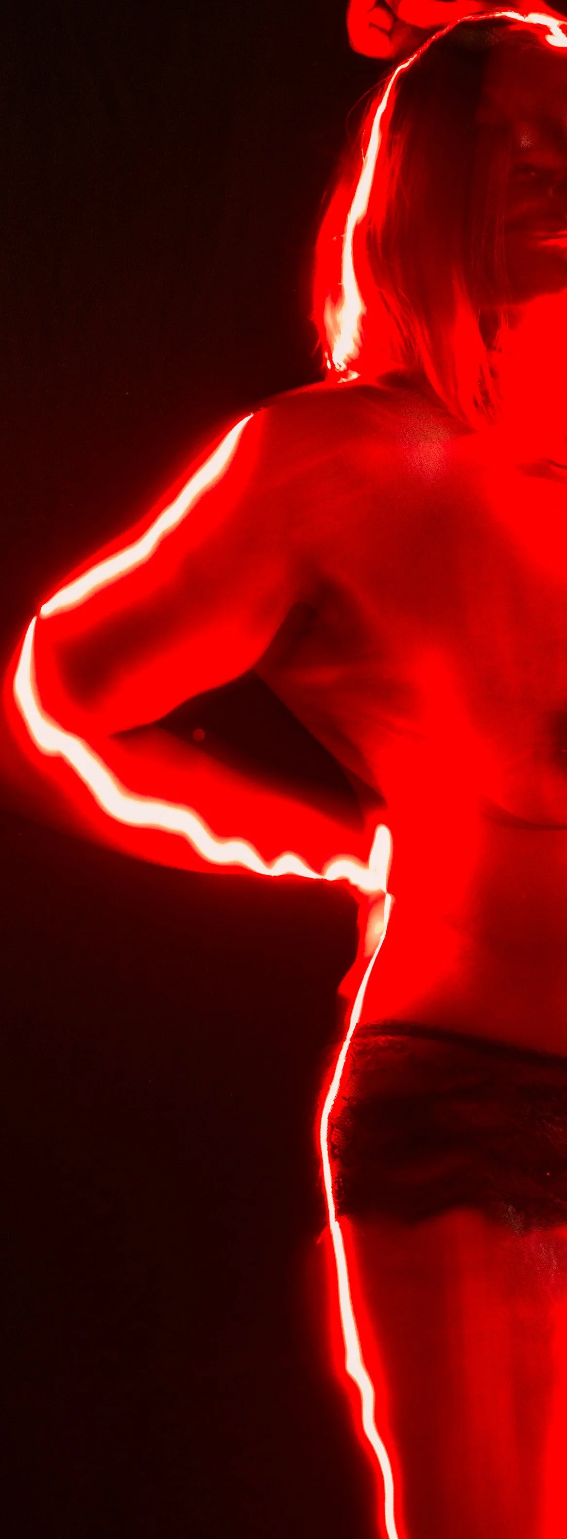 Person with blonde hair wearing black underwear, illuminated by red LED lights in a dark environment.