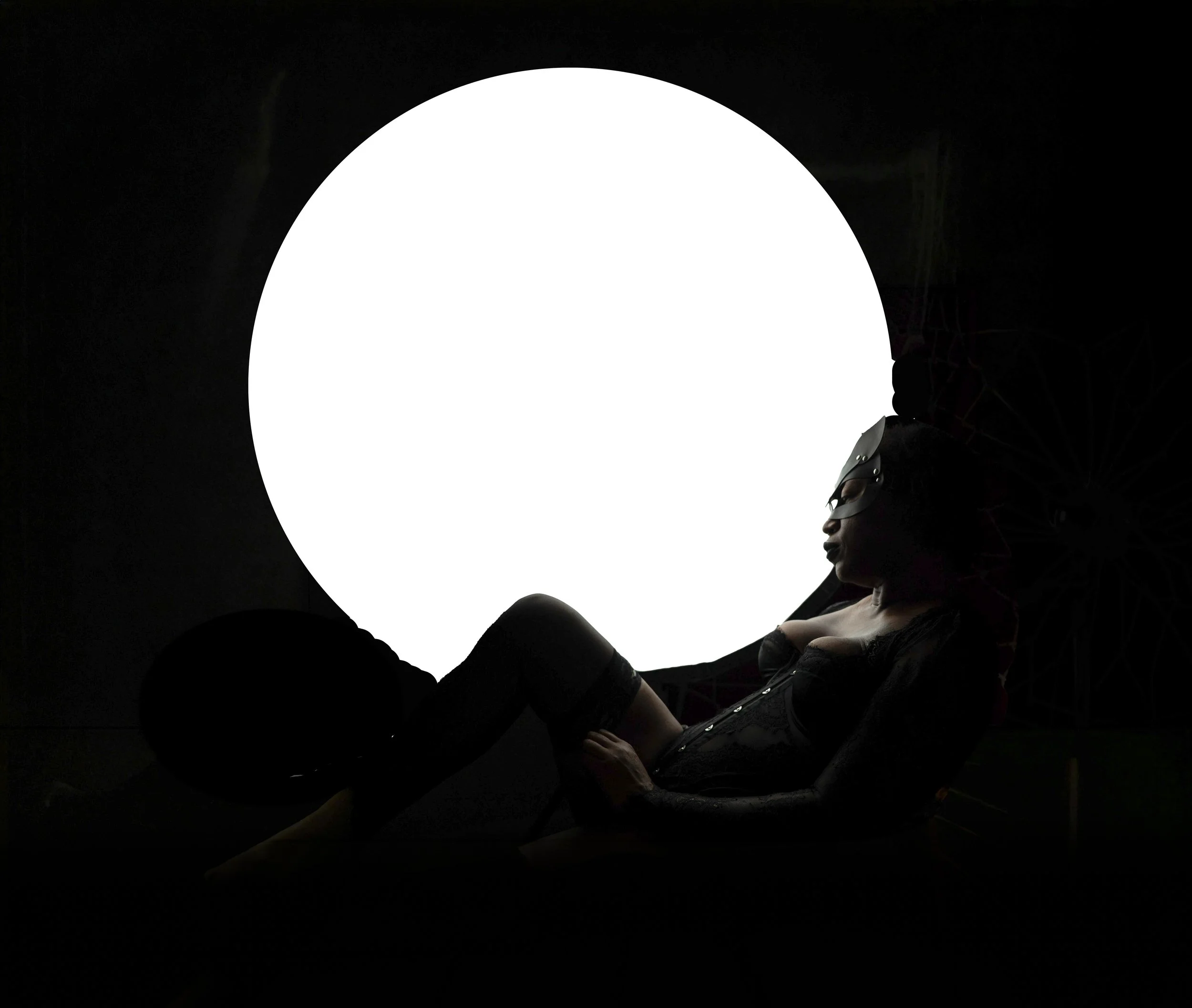Silhouette of a woman wearing glasses, lying near a large bright white circular light source in a dark room.