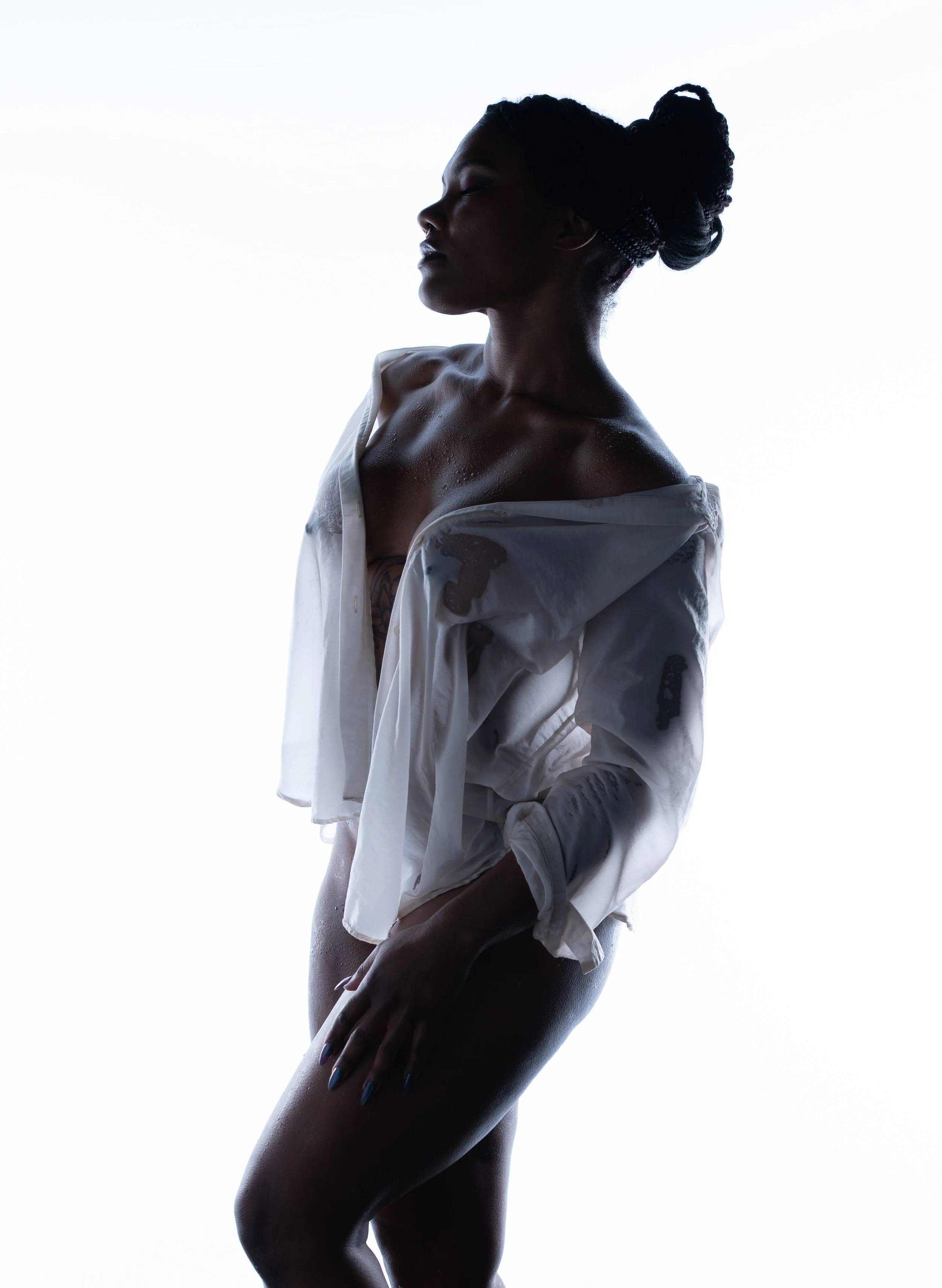 High-key silhouette portrait of a woman draped in sheer translucent fabric, shot in profile against a bright white background.