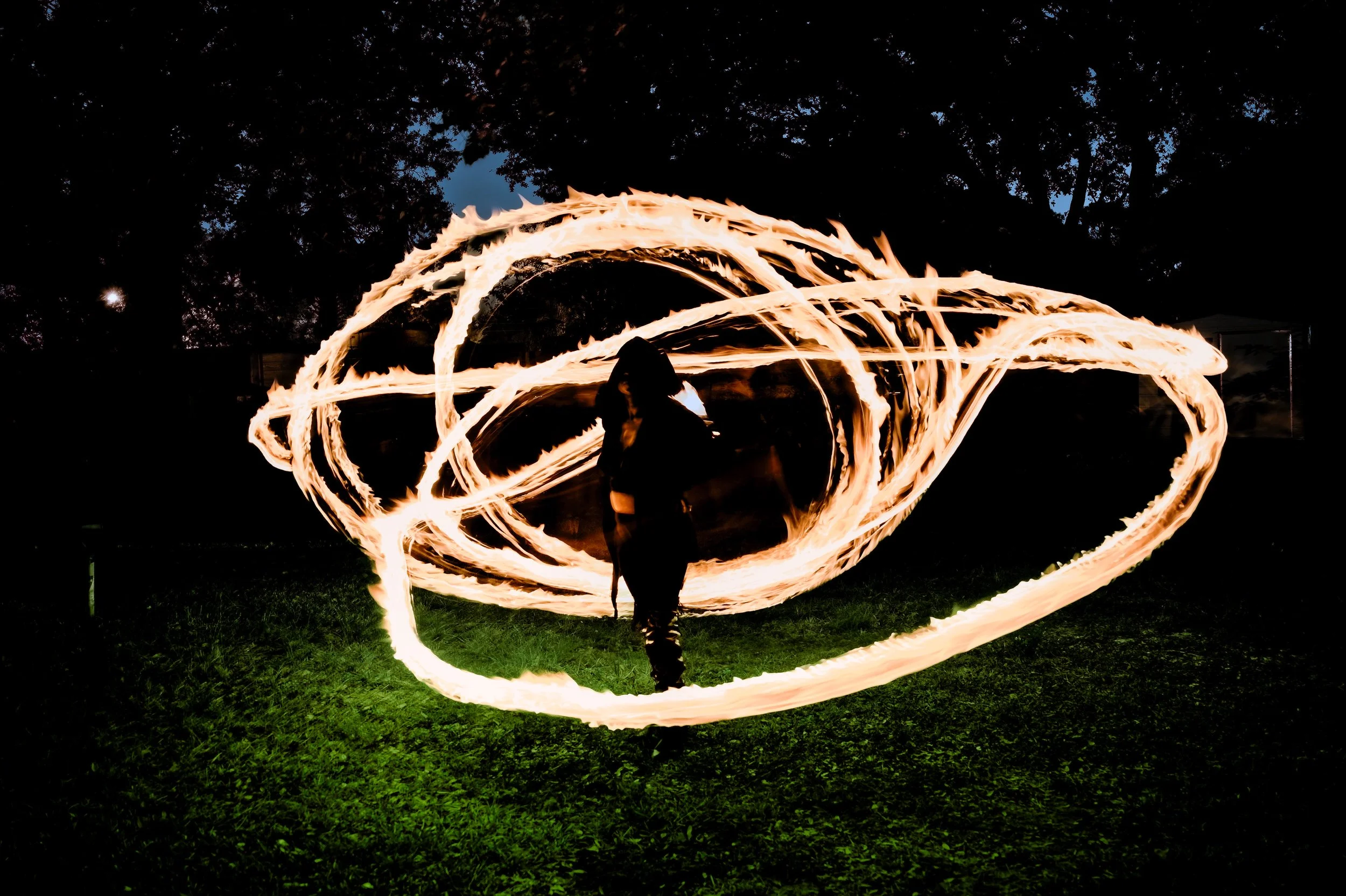 A person performing fire spinning or fire dancing in a park at night, creating swirling patterns of flames around them.