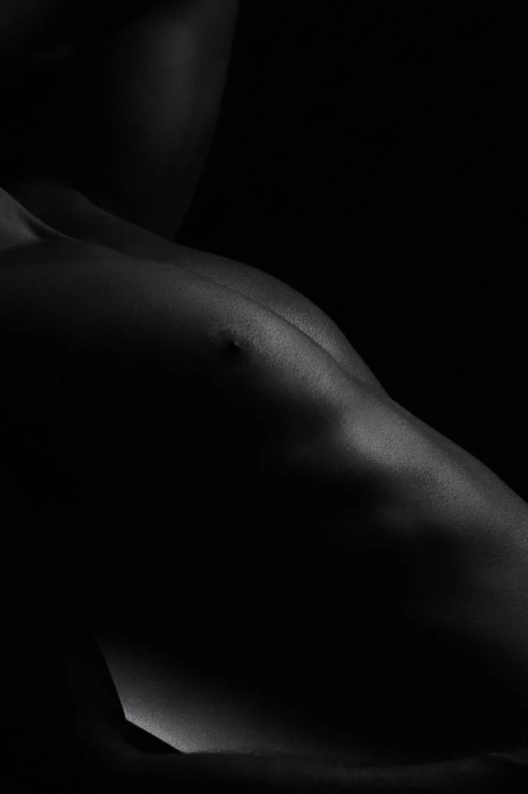 Bodyscape, Fine Art Nude.  Close-up black and white photograph of a person's torso and side, with lighting highlighting the contours of the skin and shoulder.