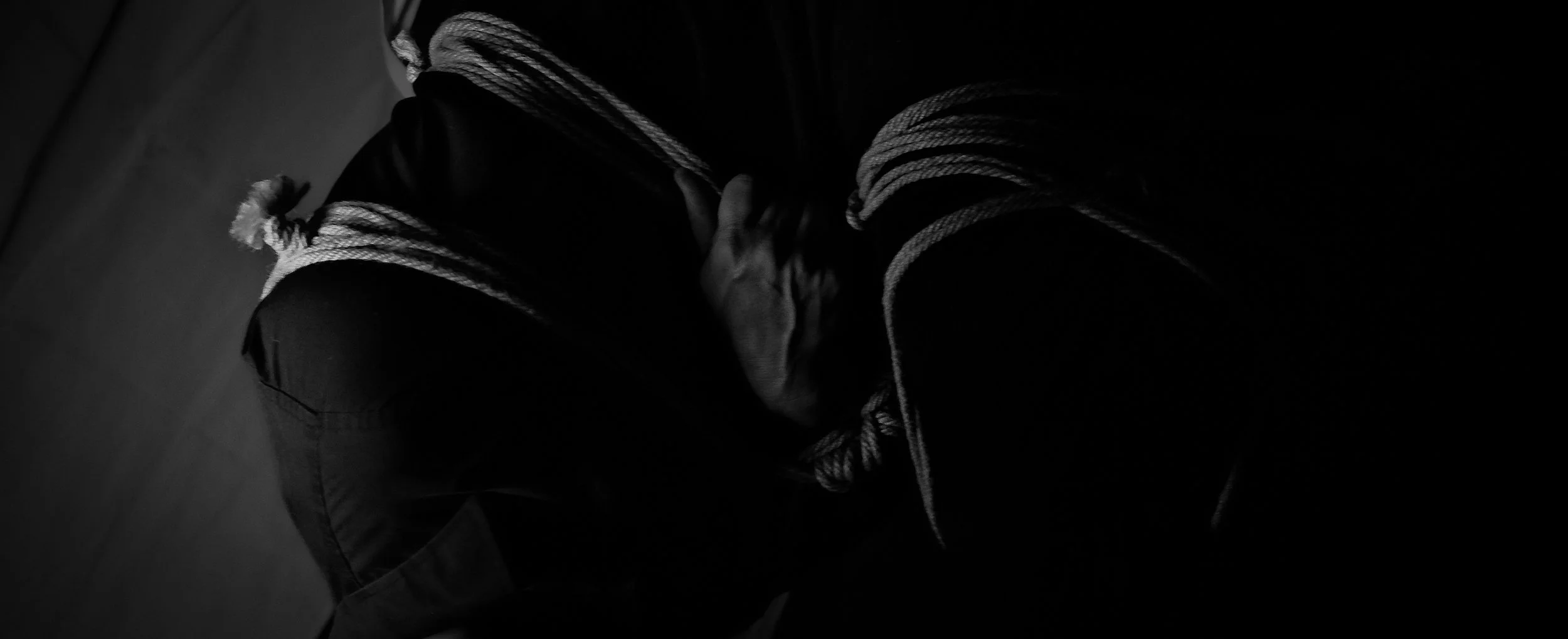 A person with their head bowed down, covering their face with their hands, in a dark setting with minimal lighting.
