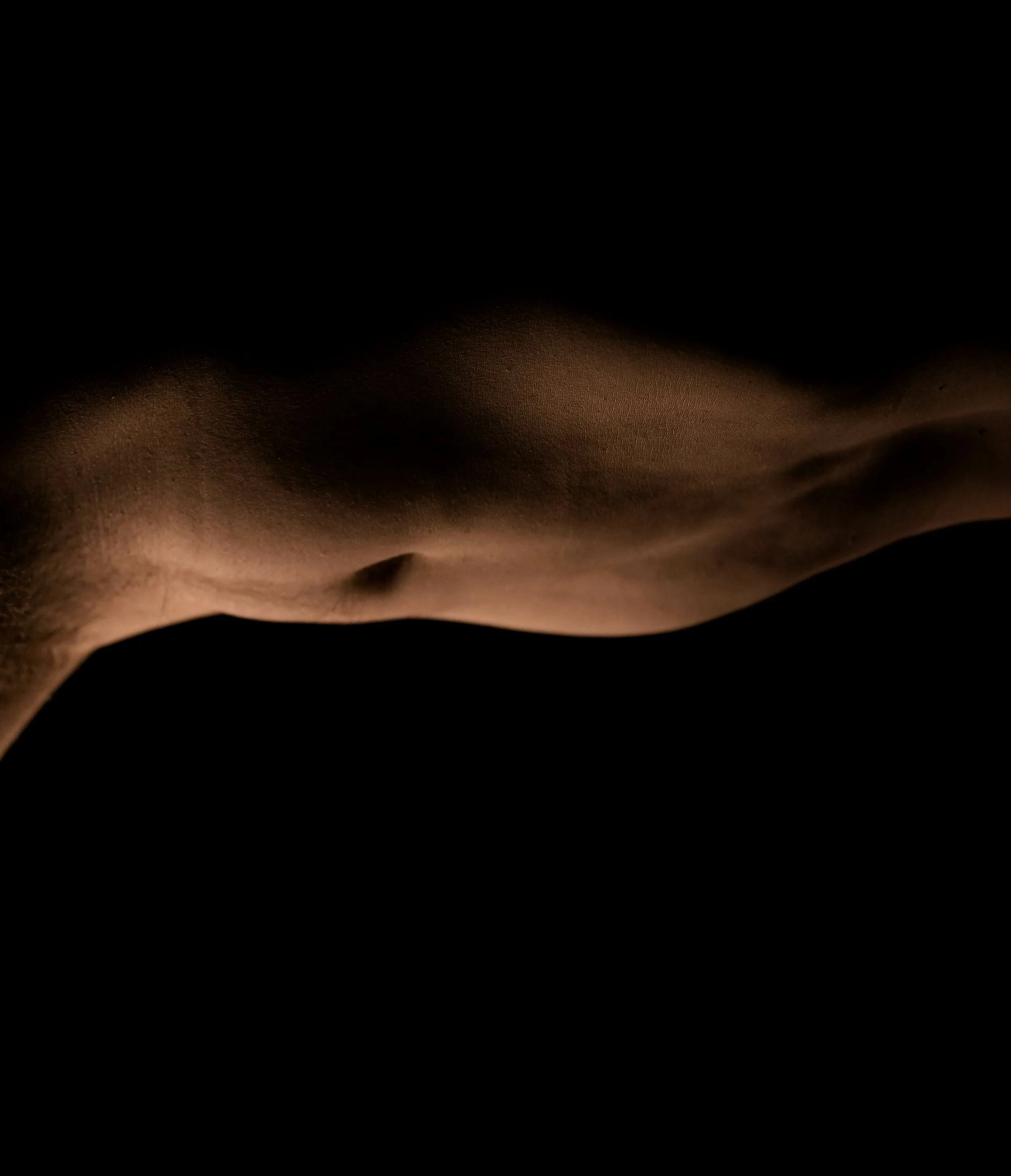 Close-up of a person's side torso, showing the chest, armpit, and abdomen, with lighting highlighting the skin's texture against a dark background.