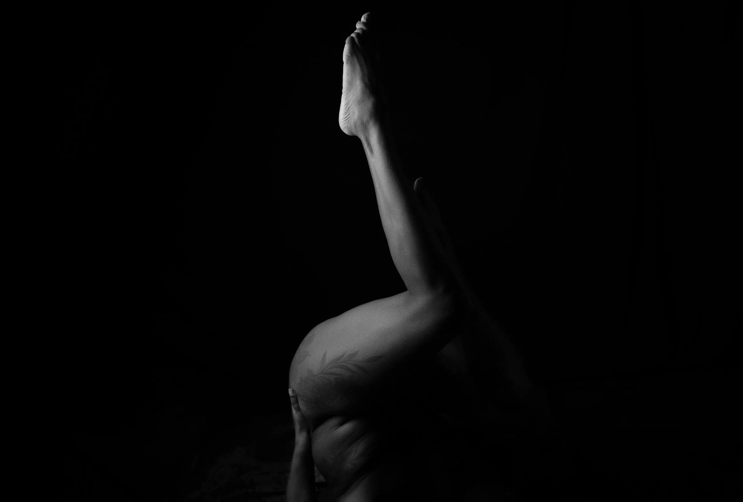 A person doing a yoga pose with one leg extended upward, captured in black and white with a dark background.