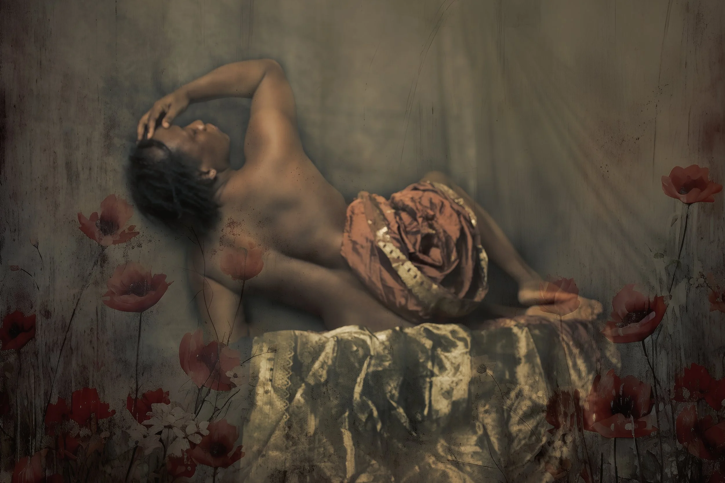 A person lying on a gold silk fabric with their arms above their head, wearing patterned clothing, surrounded by scattered red and pink flowers.