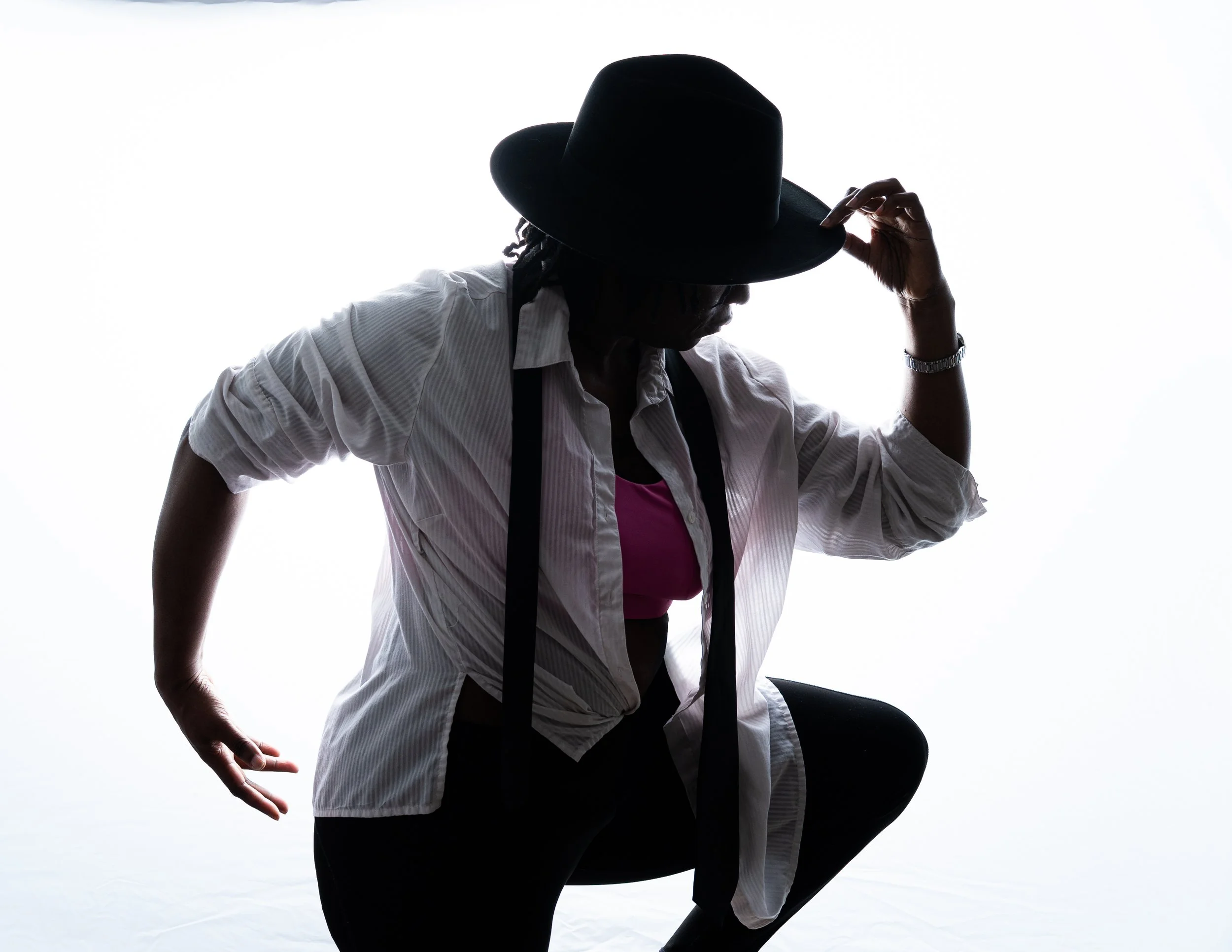 A person wearing a hat, white shirt, and pink top, seen in silhouette, is adjusting their hat with one hand, with a bright white background.
