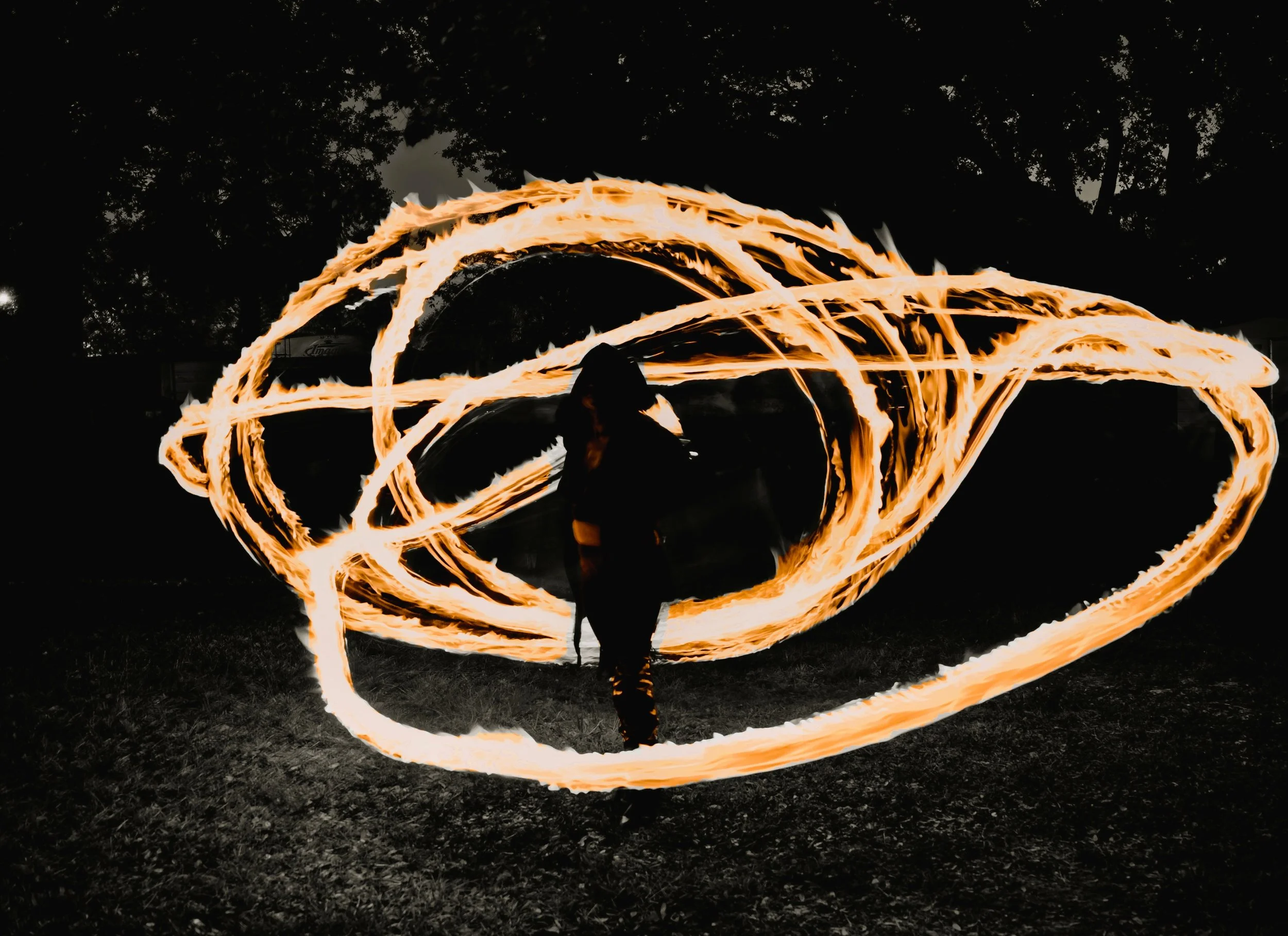 Person performing fire spinning outdoors at night, creating swirling trails of fire with a fire staff.