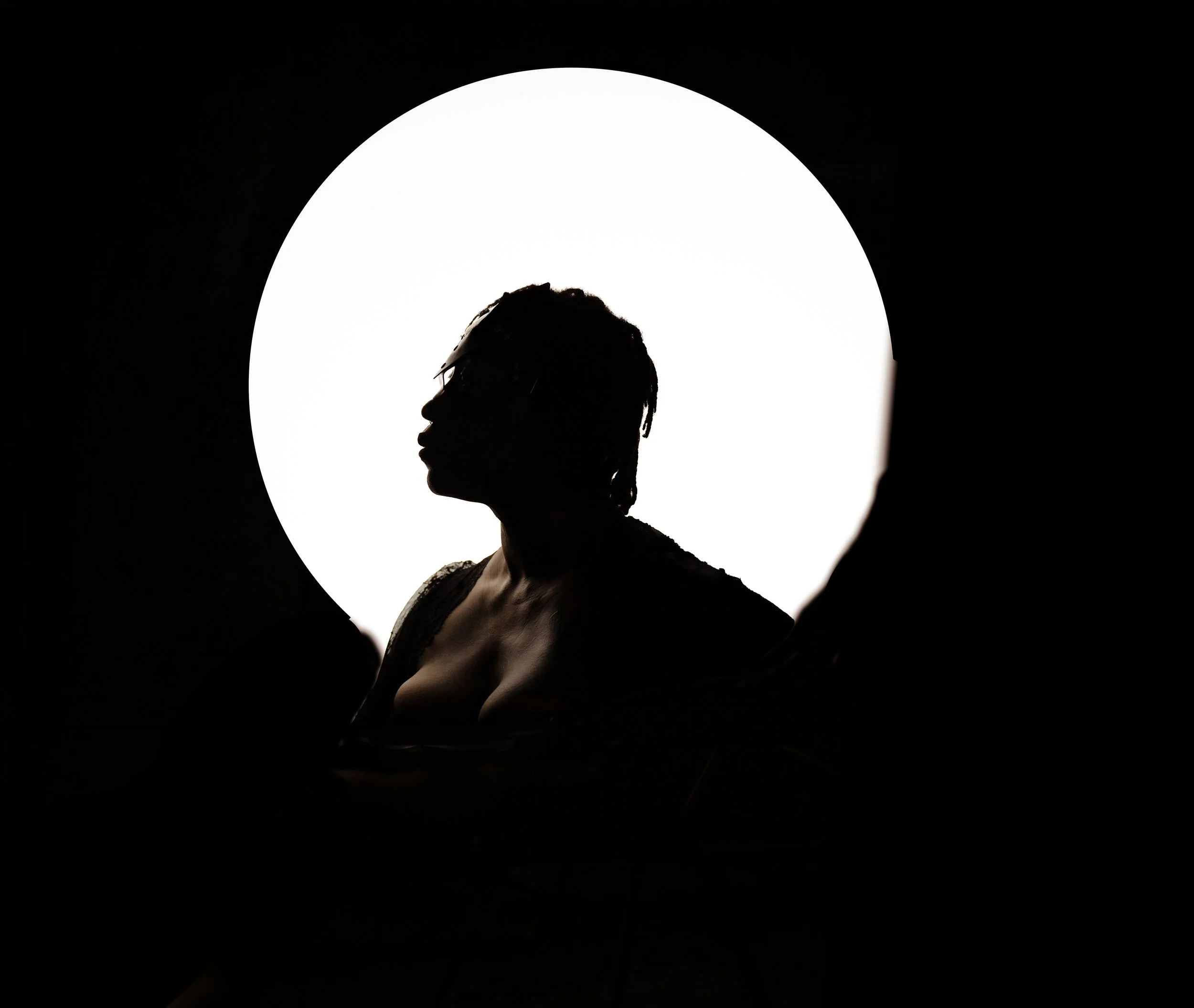 Silhouette of a woman with glasses and short hair in front of a bright circular light.