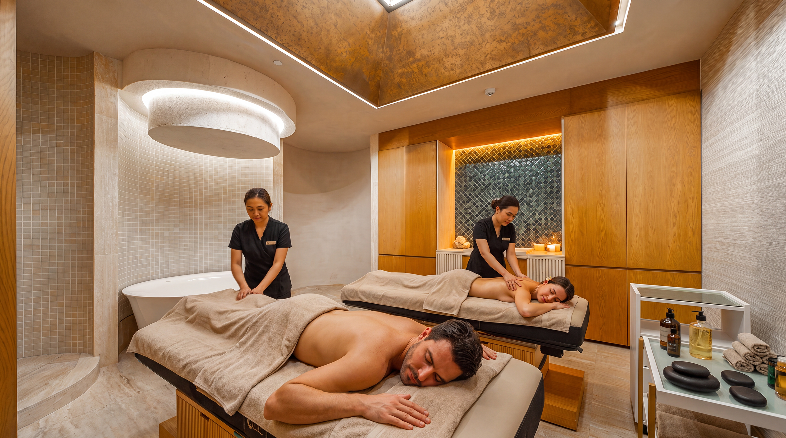 People receiving massage therapy in a spa treatment room with warm lighting, wooden accents, and candles.