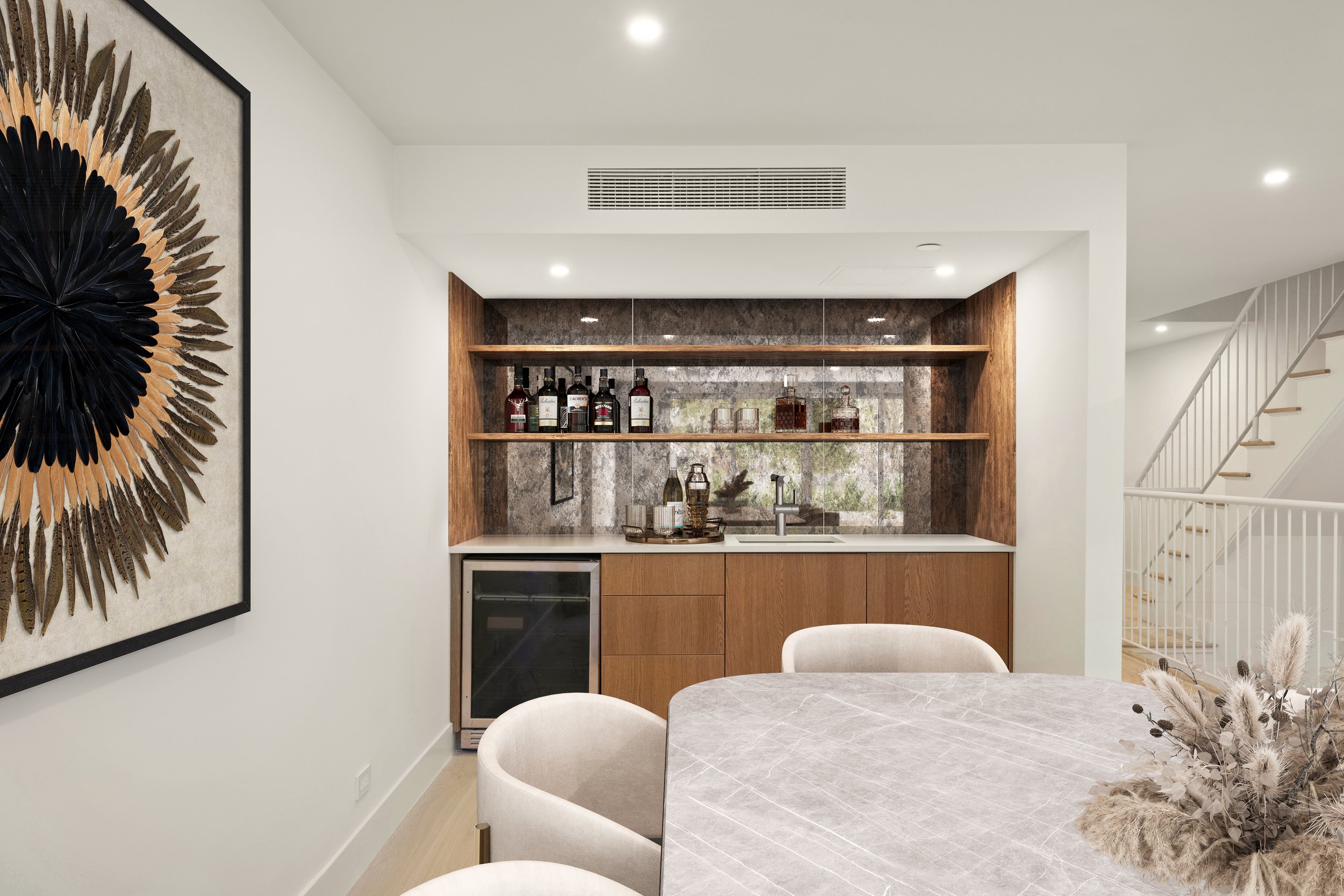 Interior view of a modern kitchen and dining area with a wooden bar, a marble table, and beige upholstered chairs, featuring a decorative wall art piece on the left.