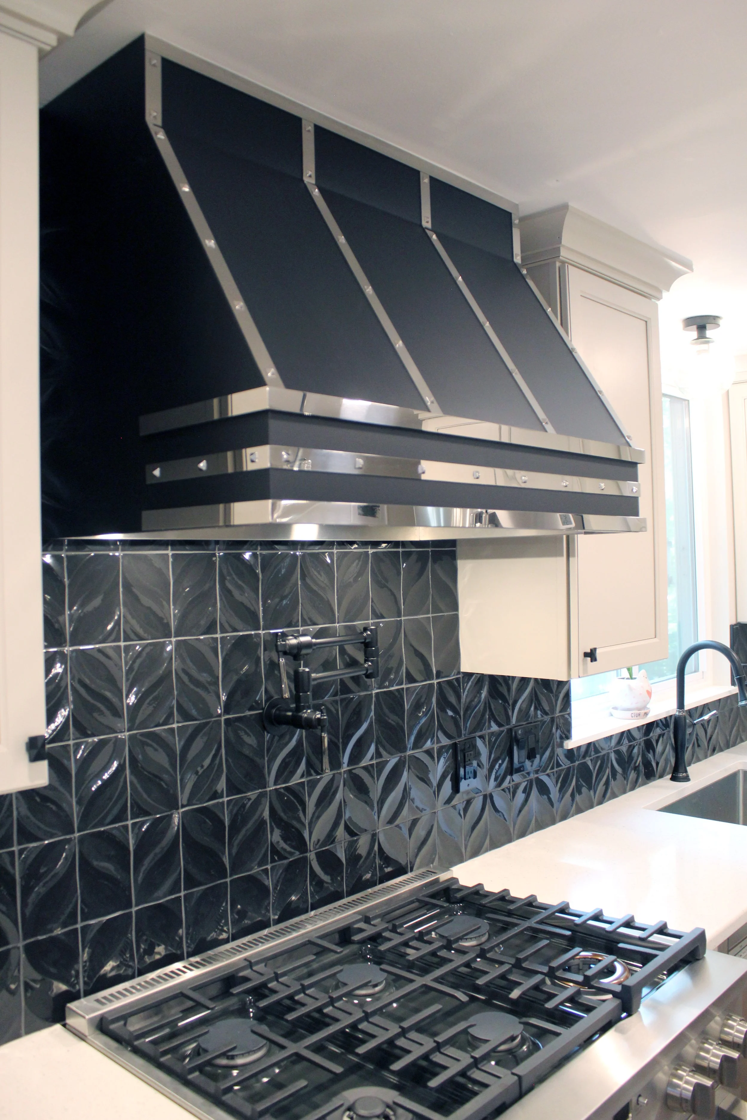 Modern kitchen with black tiled backsplash, stovetop, and black range hood.