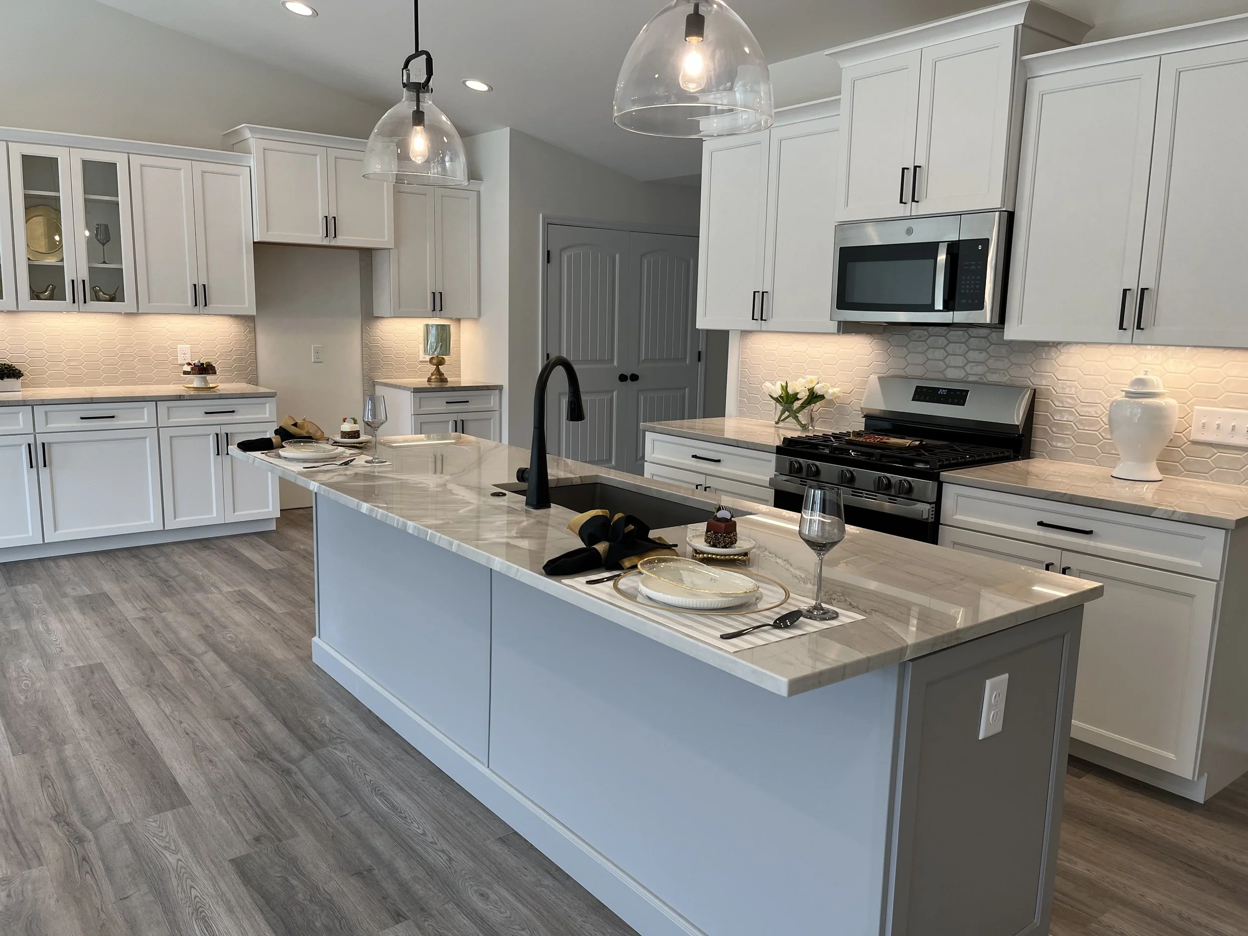 Modern kitchen with white cabinets, a marble island, stainless steel microwave, stove, and pendant lighting fixtures.