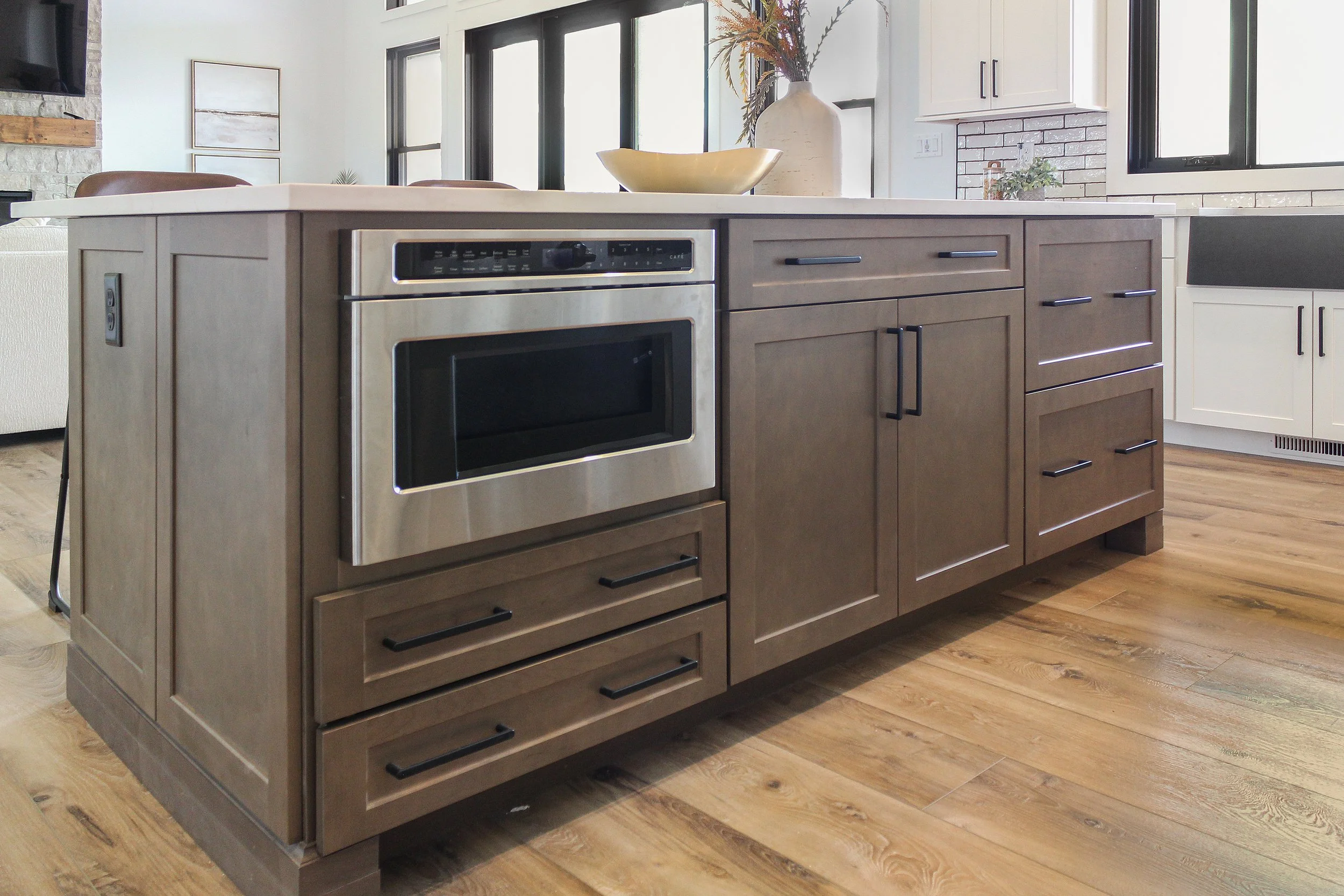 Modern kitchen island with a microwave, brown cabinets, and countertop decor, in an open-concept kitchen.