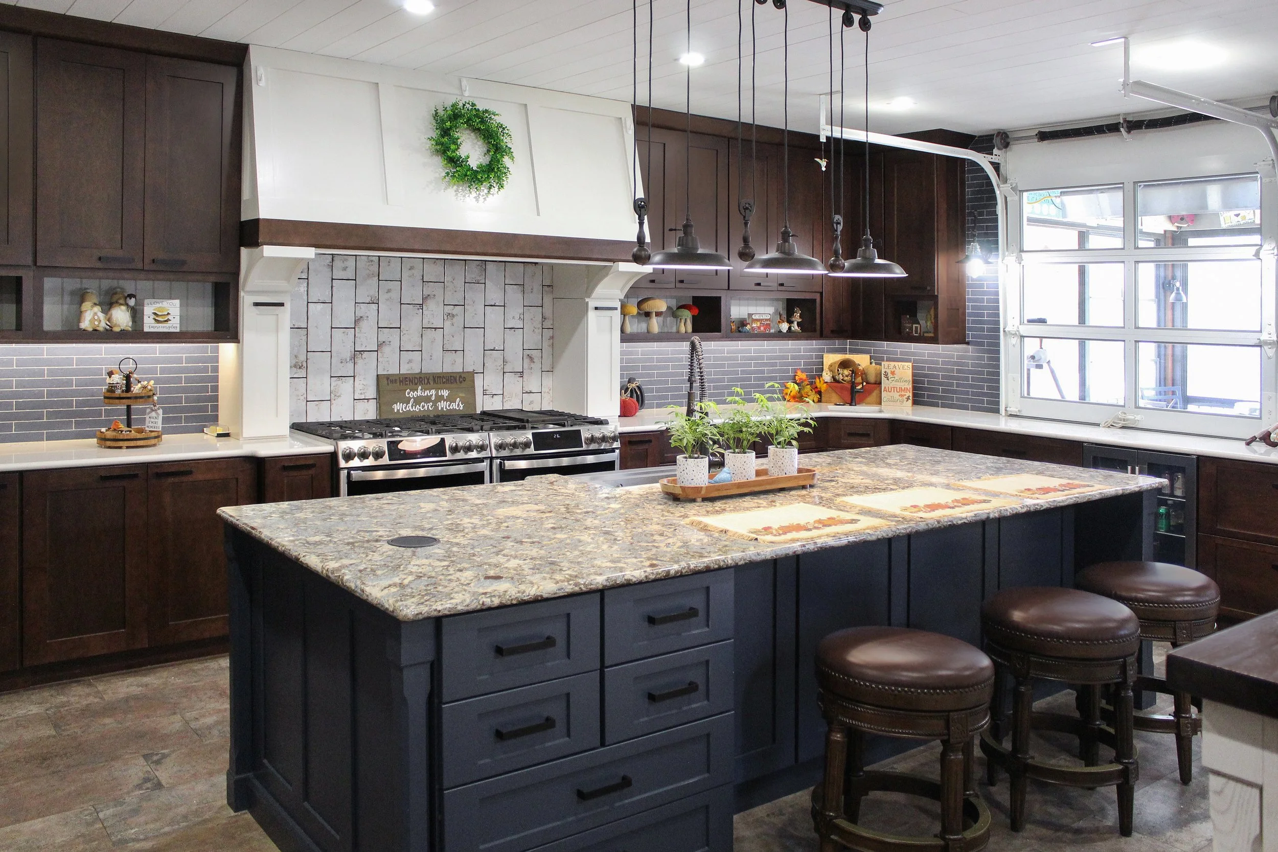 Modern kitchen with dark cabinetry, granite island, stainless steel appliances, and large windows.