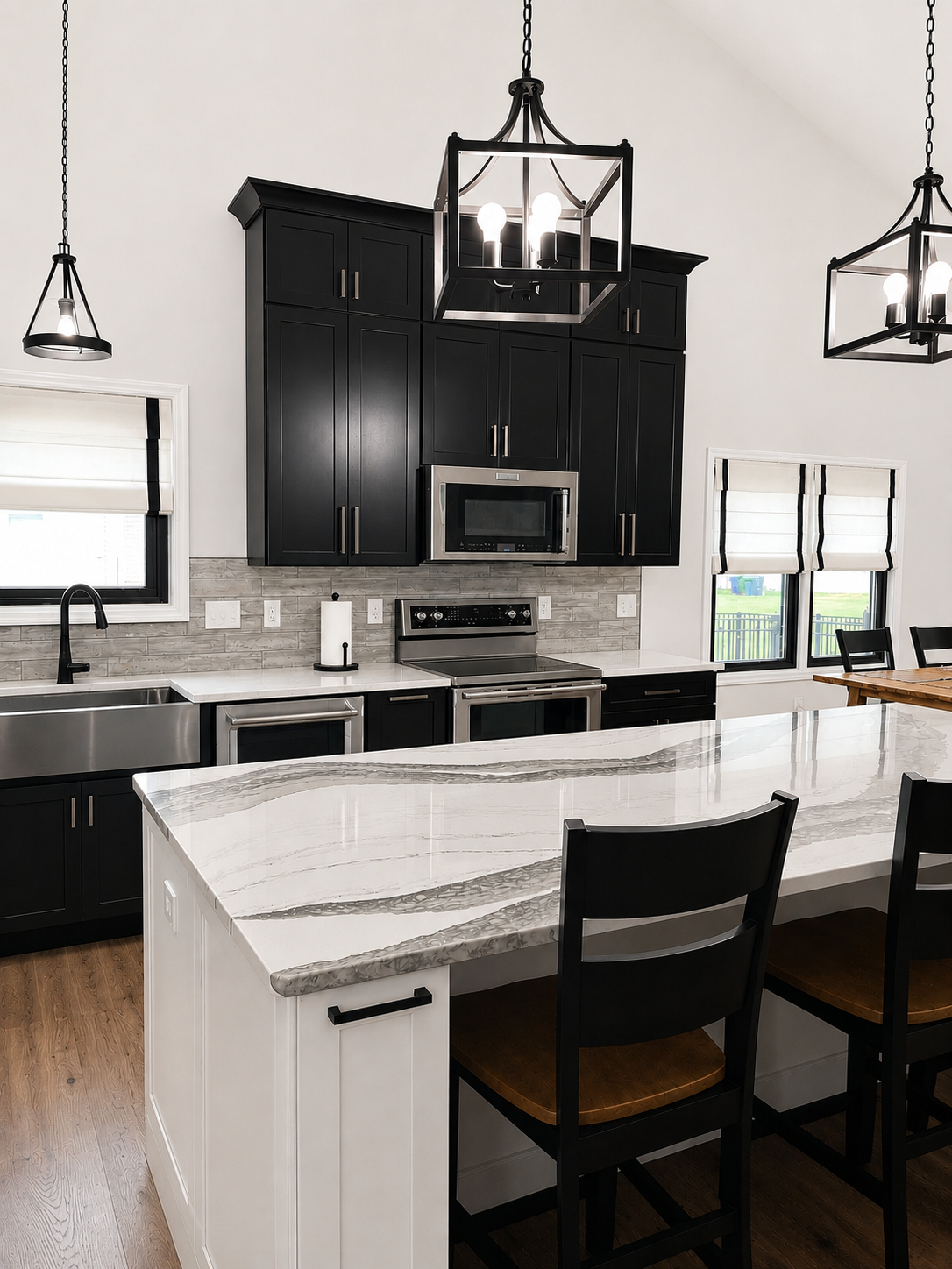Modern kitchen with black cabinets, stainless steel appliances, marble countertop island, black chairs, and pendant lighting.