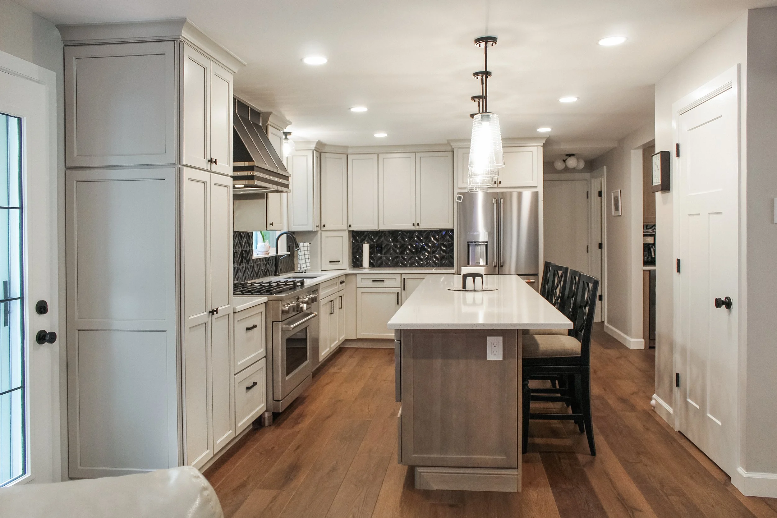 A modern kitchen with white cabinetry, a large island with barstools, stainless steel appliances, and pendant lighting.