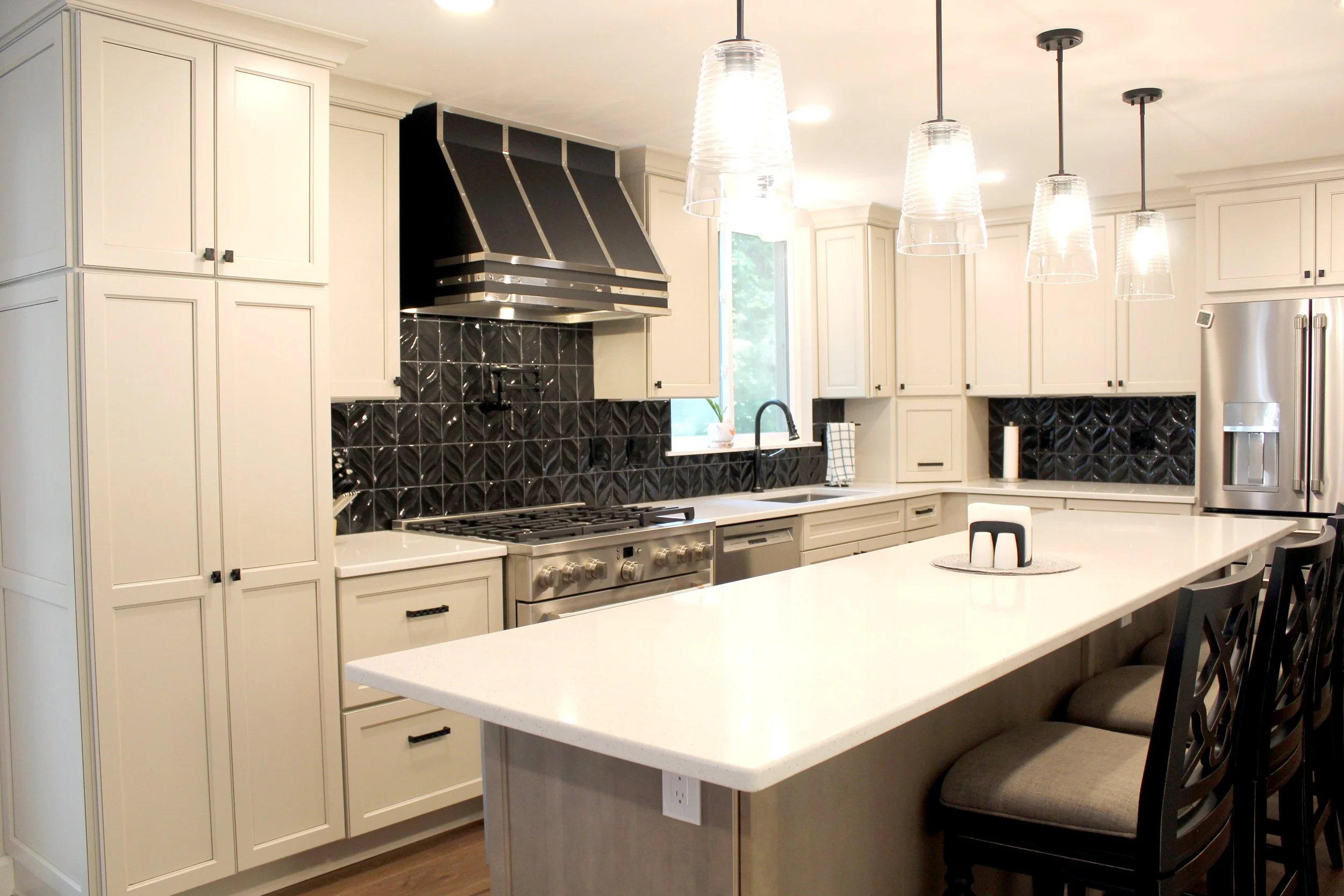 Modern kitchen with white cabinetry, a large island, black textured backsplash, stainless steel appliances, pendant lights, and bar stools.