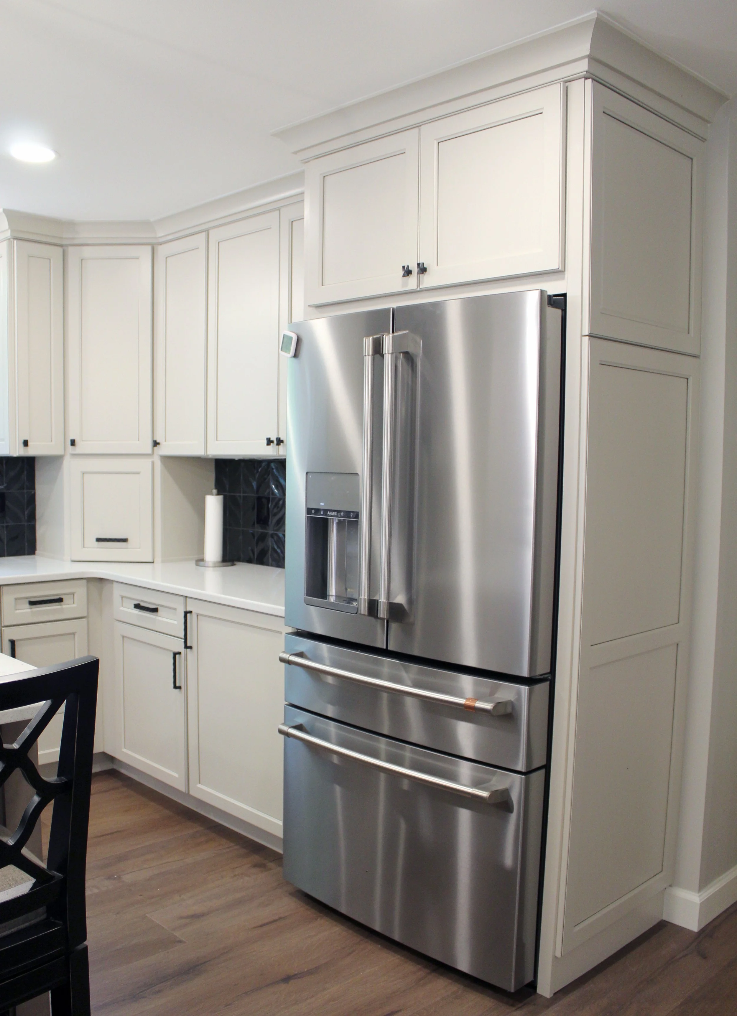 Stainless steel refrigerator in a modern kitchen with white cabinets and black hardware.