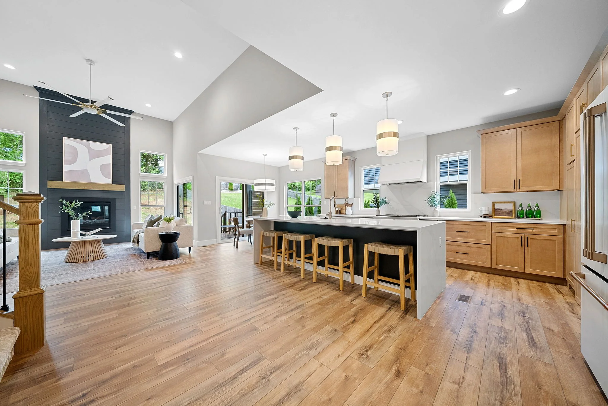 Open-concept living room and kitchen with hardwood floors, modern furniture, a fireplace, and large windows.