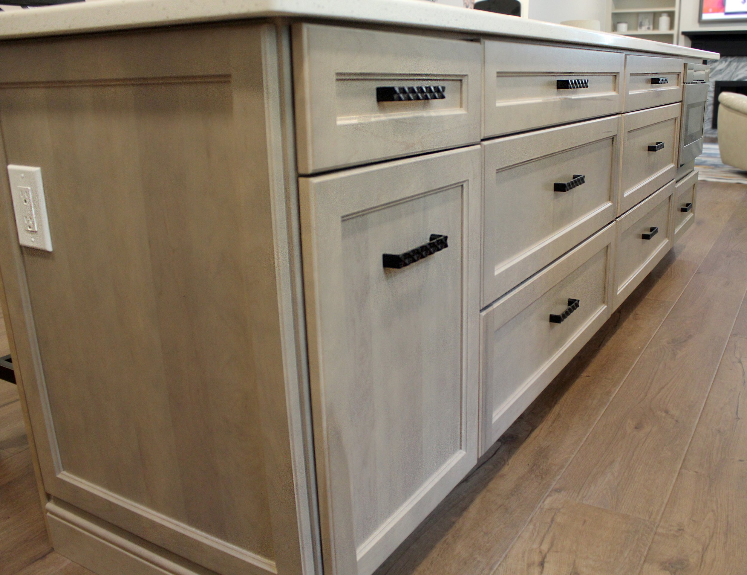 A beige kitchen island with multiple drawers and black handles, situated on a wooden floor.