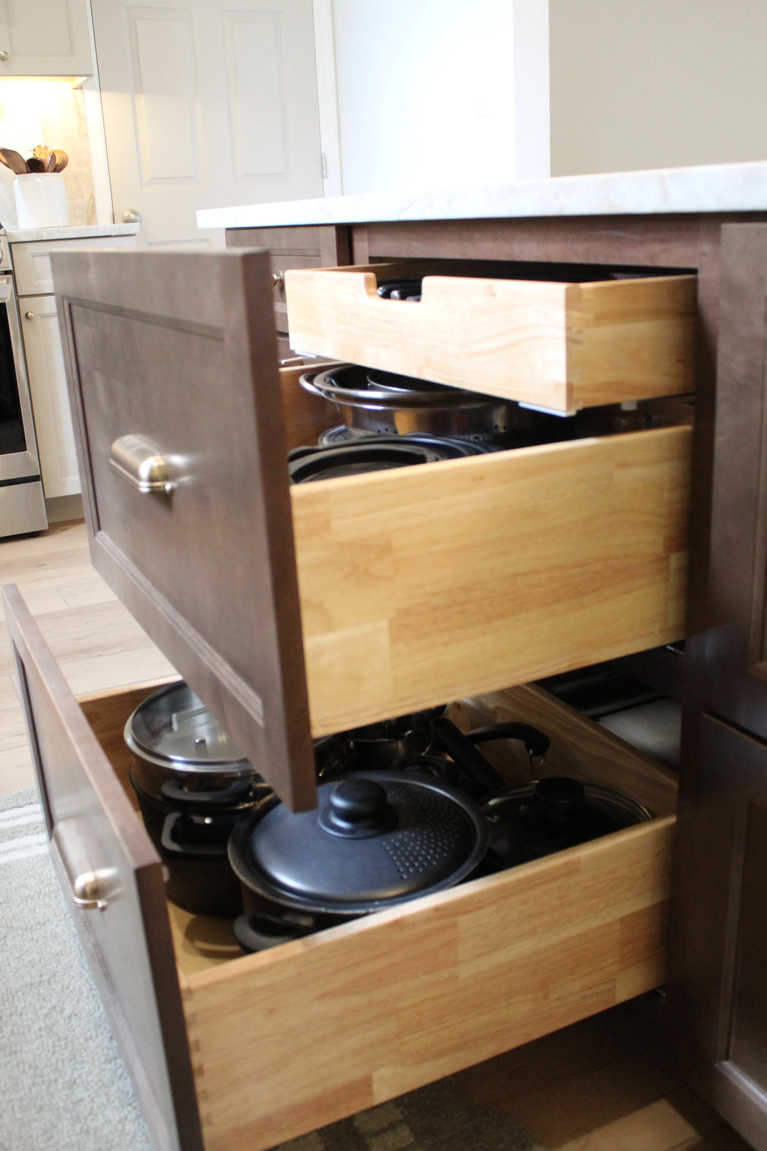 Kitchen drawer partially open revealing stacked pots and pans inside.