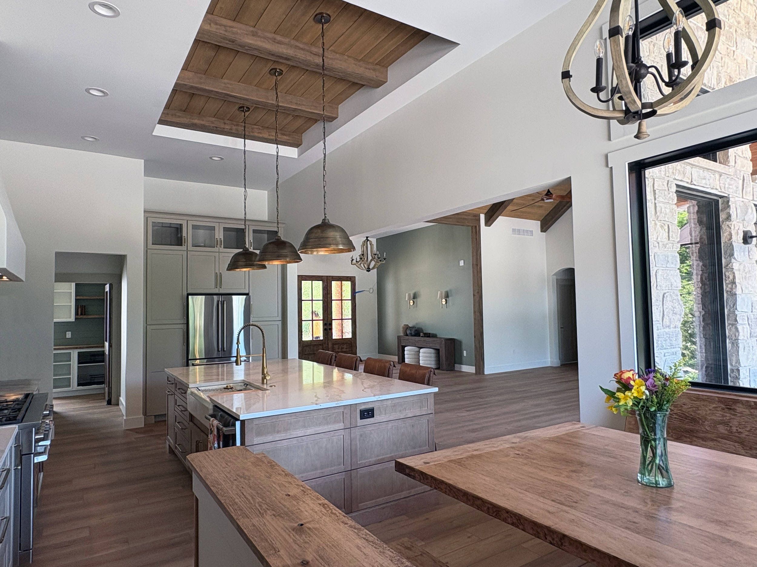Open-concept kitchen and dining area with a wooden island, pendant lights, large window, sliding glass door, and vaulted wooden ceiling.