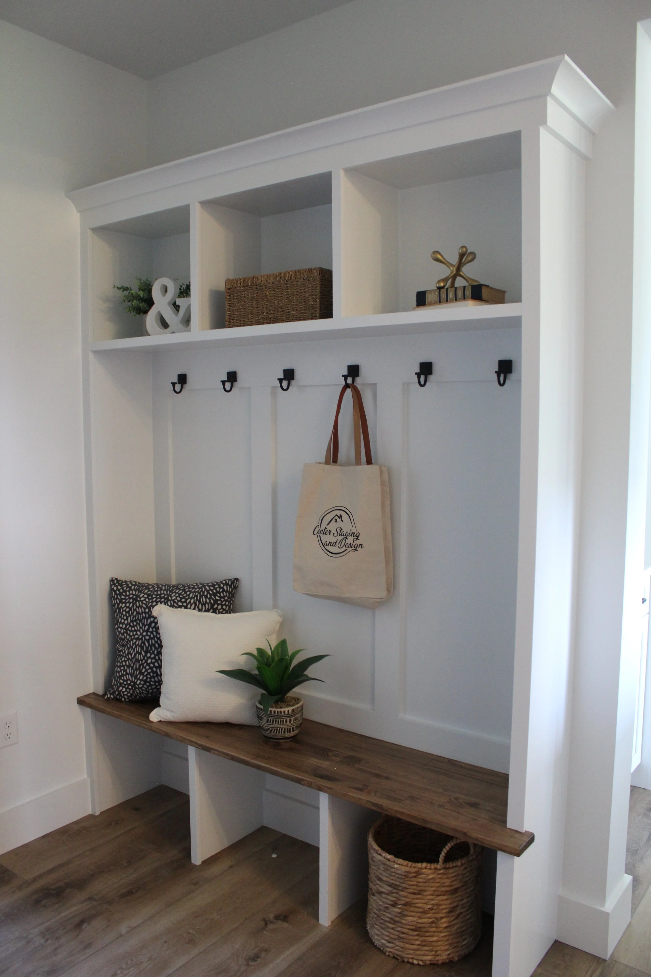 Entryway with a built-in white shelving unit, a wooden bench with cushions, a small potted plant, and a woven basket.