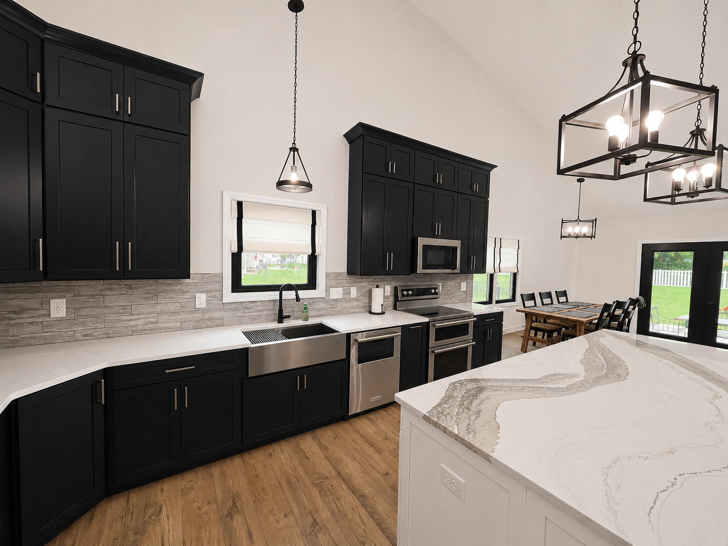 Modern kitchen with black cabinets, stainless steel appliances, a white marble island, hardwood floors, and a dining area with black chairs and table.