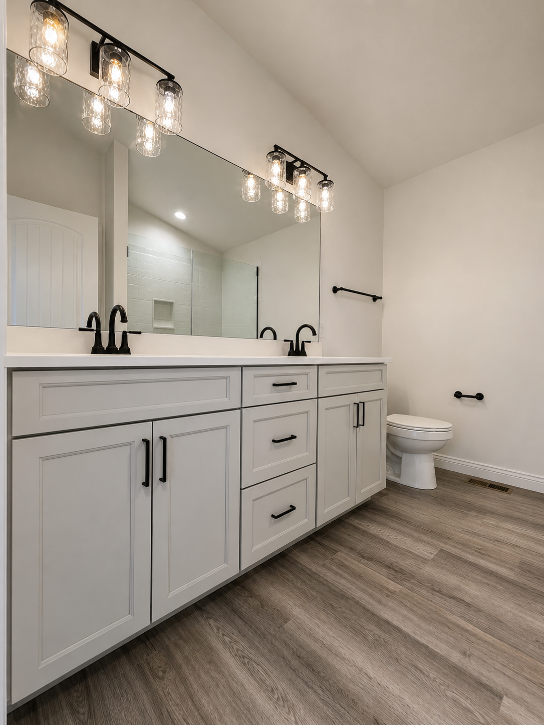 Modern bathroom with white vanity, black fixtures, large mirror, and a toilet, with wood-look flooring.