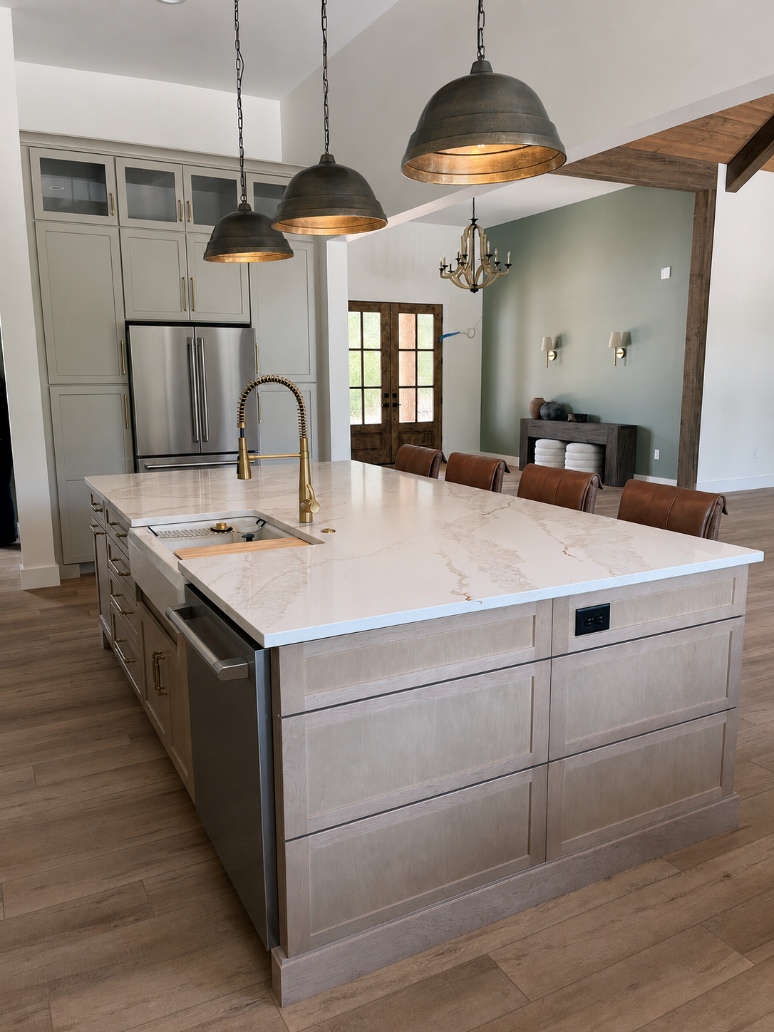 Modern kitchen with a large white marble island, brass fixtures, black pendulum lights, stainless steel appliances, and a wooden floor.