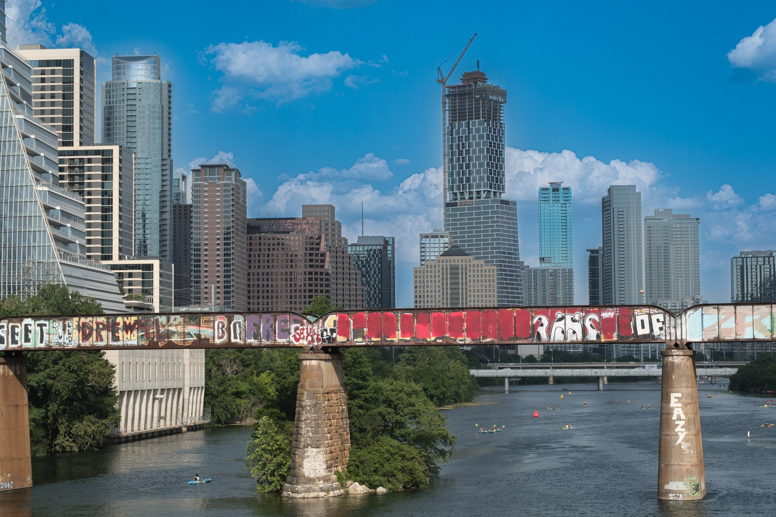 A graffiti-covered freight crosses the trestle with downtown behind it.