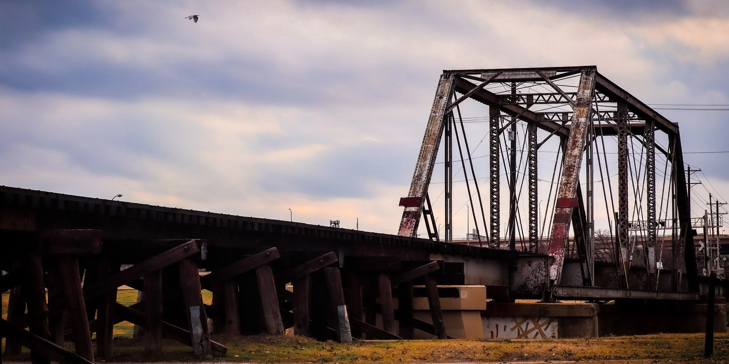 An old rail truss bridge silhouetted over the water.