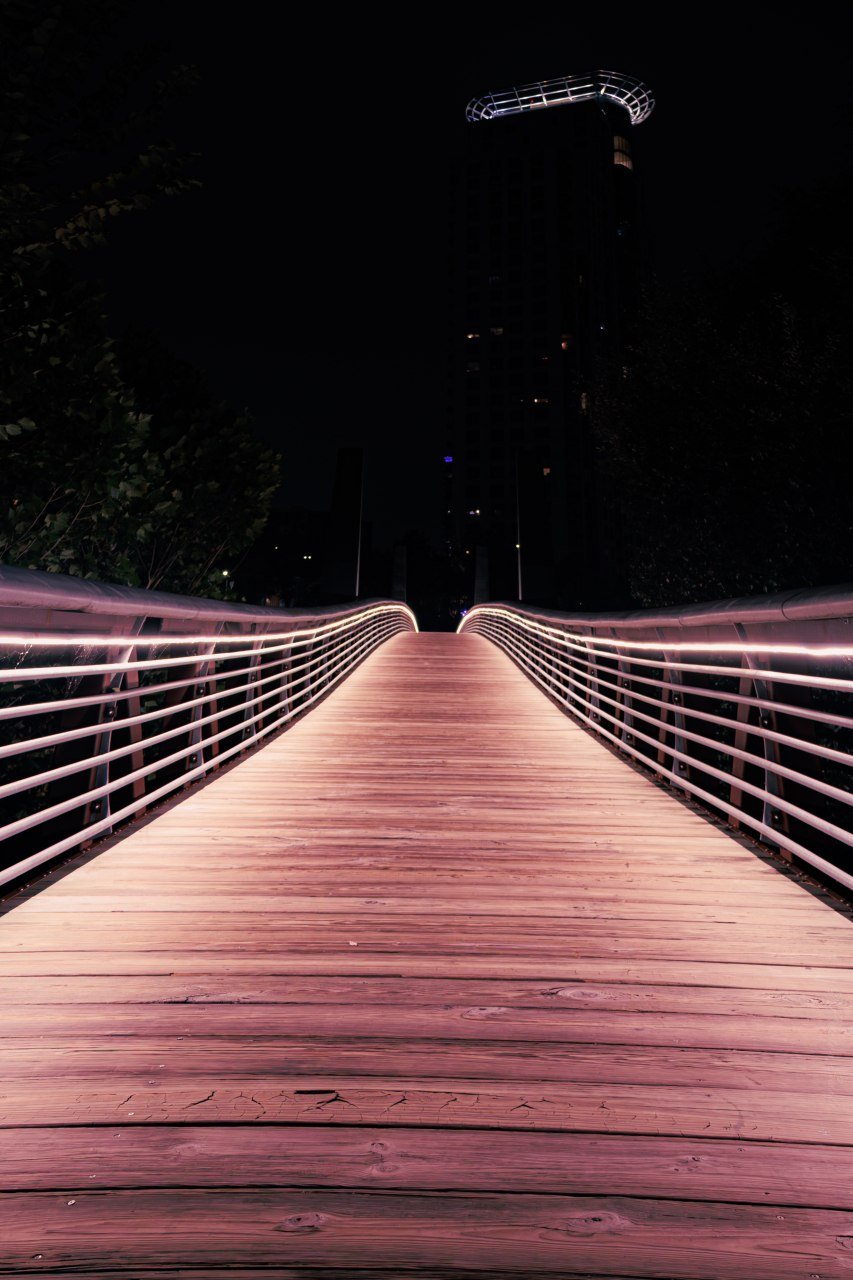 A pedestrian bridge over the bayou lit up like a neon sign.