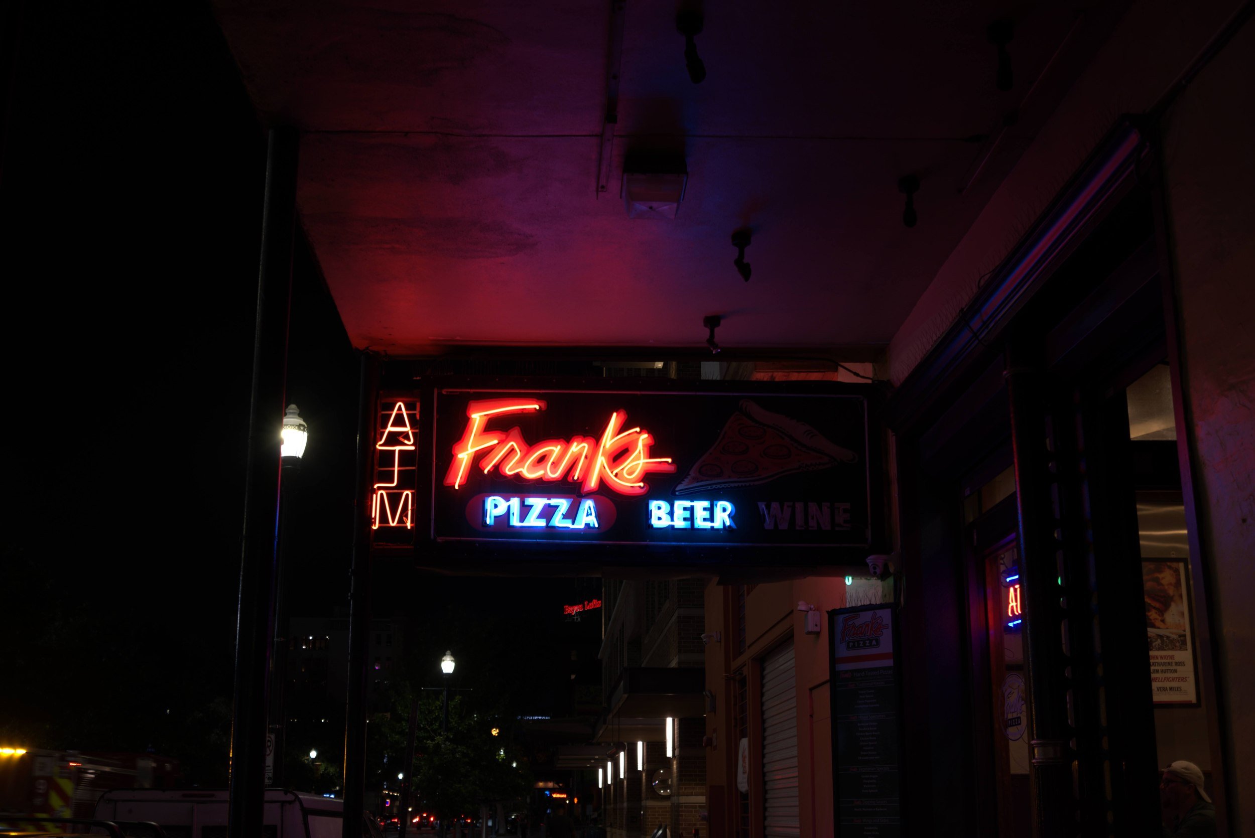 Neon pizza and beer on a quiet downtown corner.