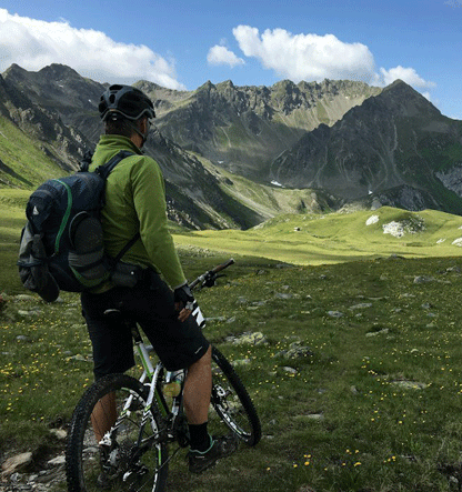 Persona en bicicleta en un paisaje de montañas verdes y cielos azules.