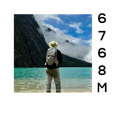 Persona con sombrero y mochila observando un lago azul rodeado de montañas y nubes.