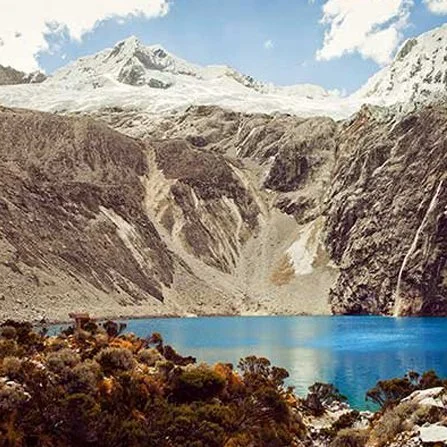 Lago azul rodeado de montañas rocosas y picos nevados bajo un cielo con algunas nubes.