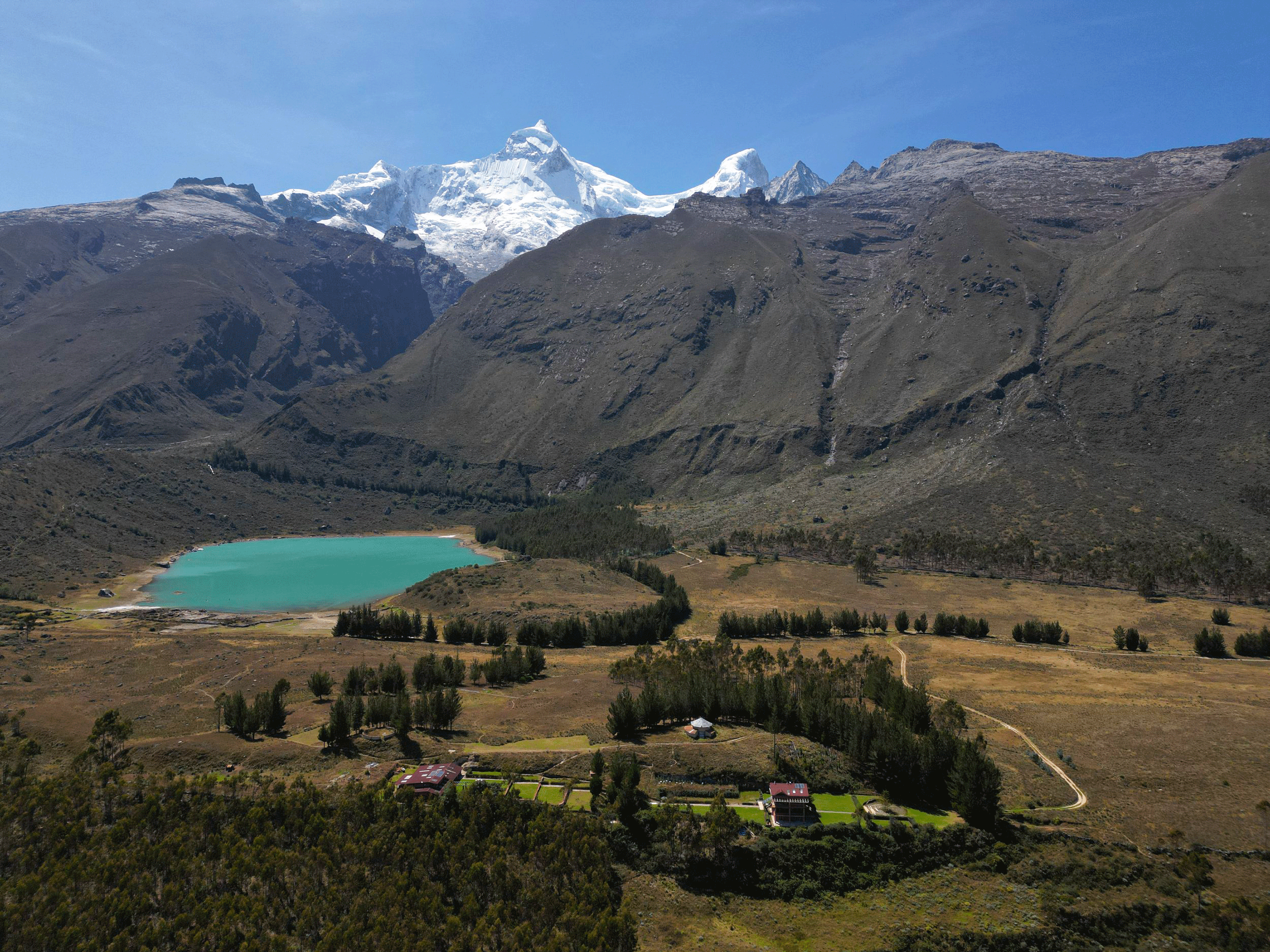Montañas nevadas y un lago azul turquesa rodeado de vegetación y casas en un paisaje natural.