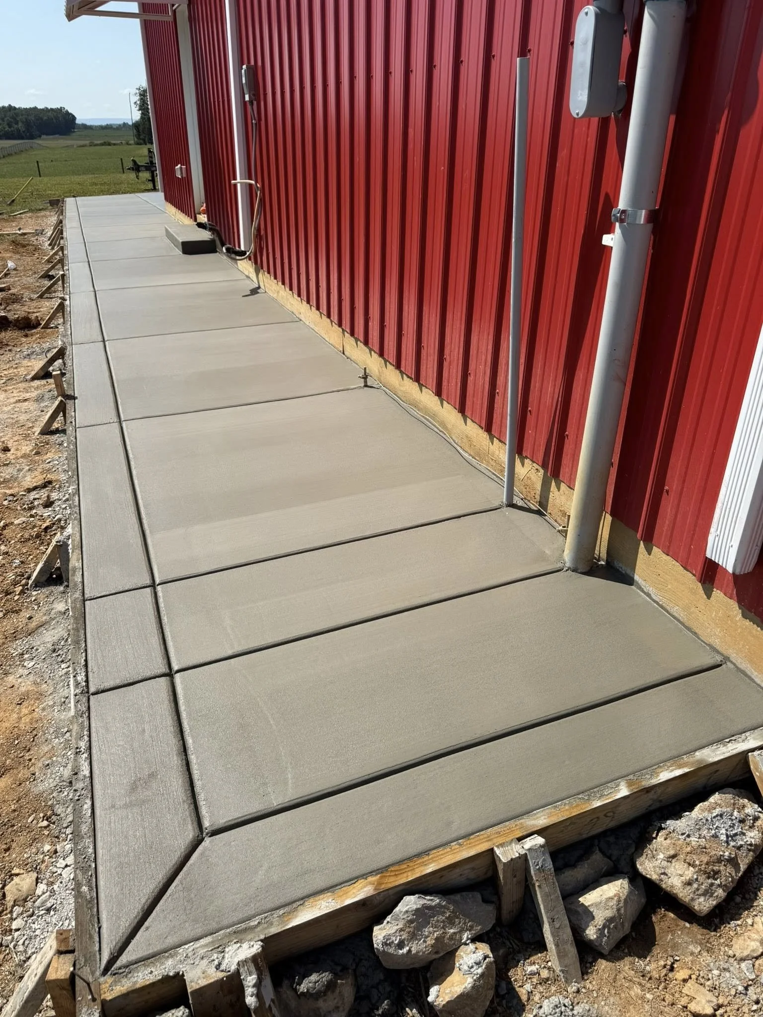 Freshly poured concrete pad with crisp tooled control joints running alongside a red metal building, finished smooth and ready for use.