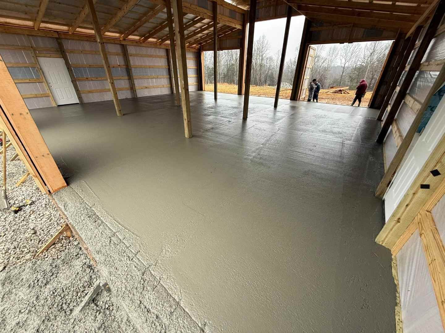 Freshly poured concrete slab inside a pole barn shop, smooth-finished from wall to wall and ready for equipment, vehicles, or storage use.