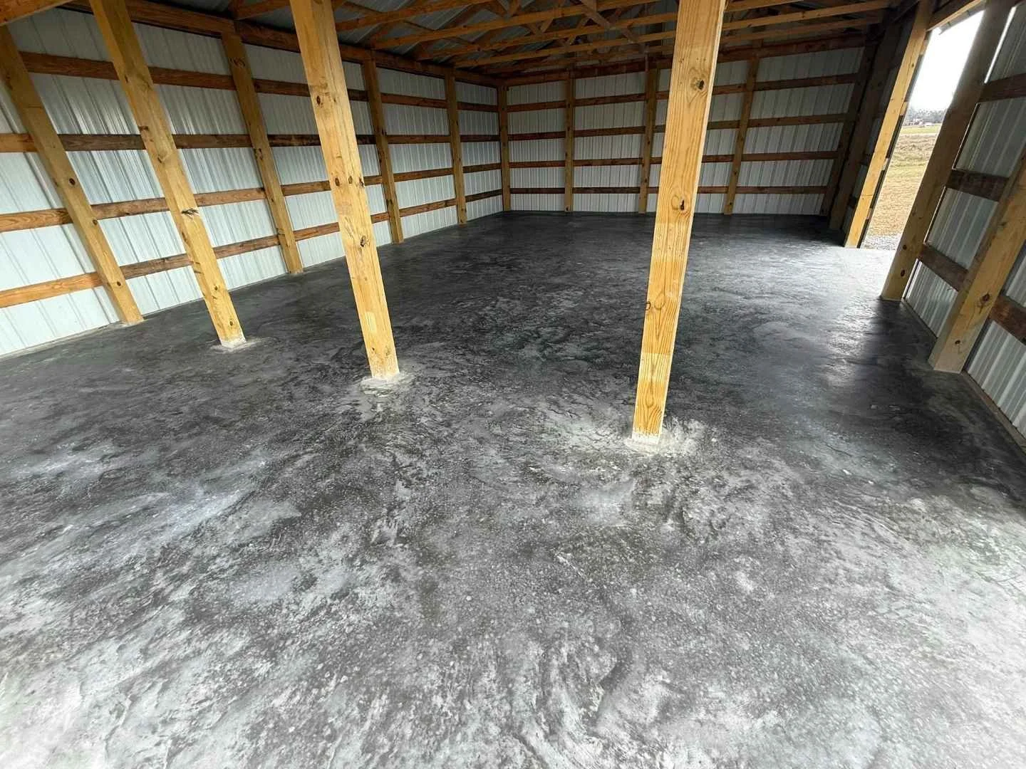 Finished concrete slab foundation inside a metal pole barn with wood support posts